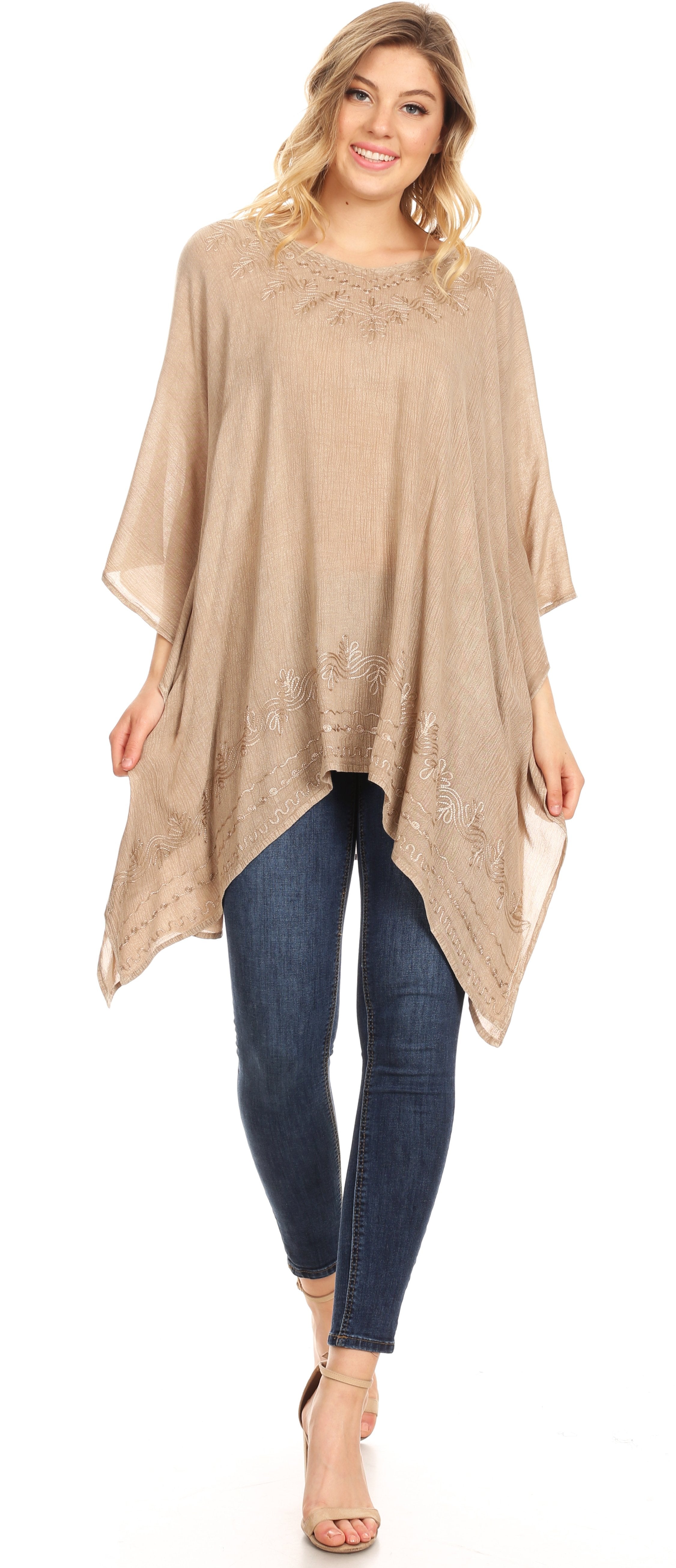 Woman wearing a beige poncho over blue jeans on a white background
