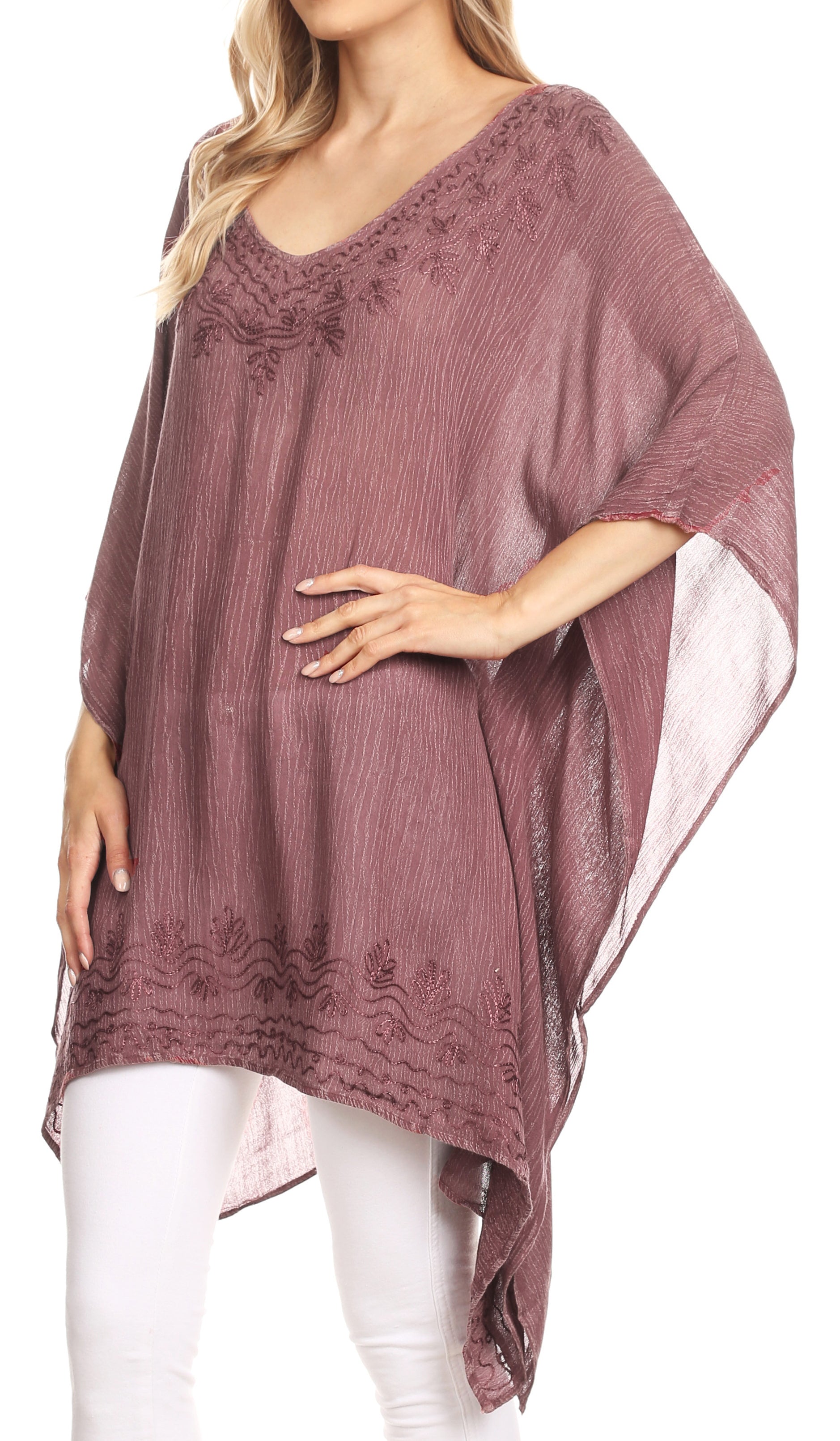 Woman wearing a mauve poncho with floral embroidery on a white background
