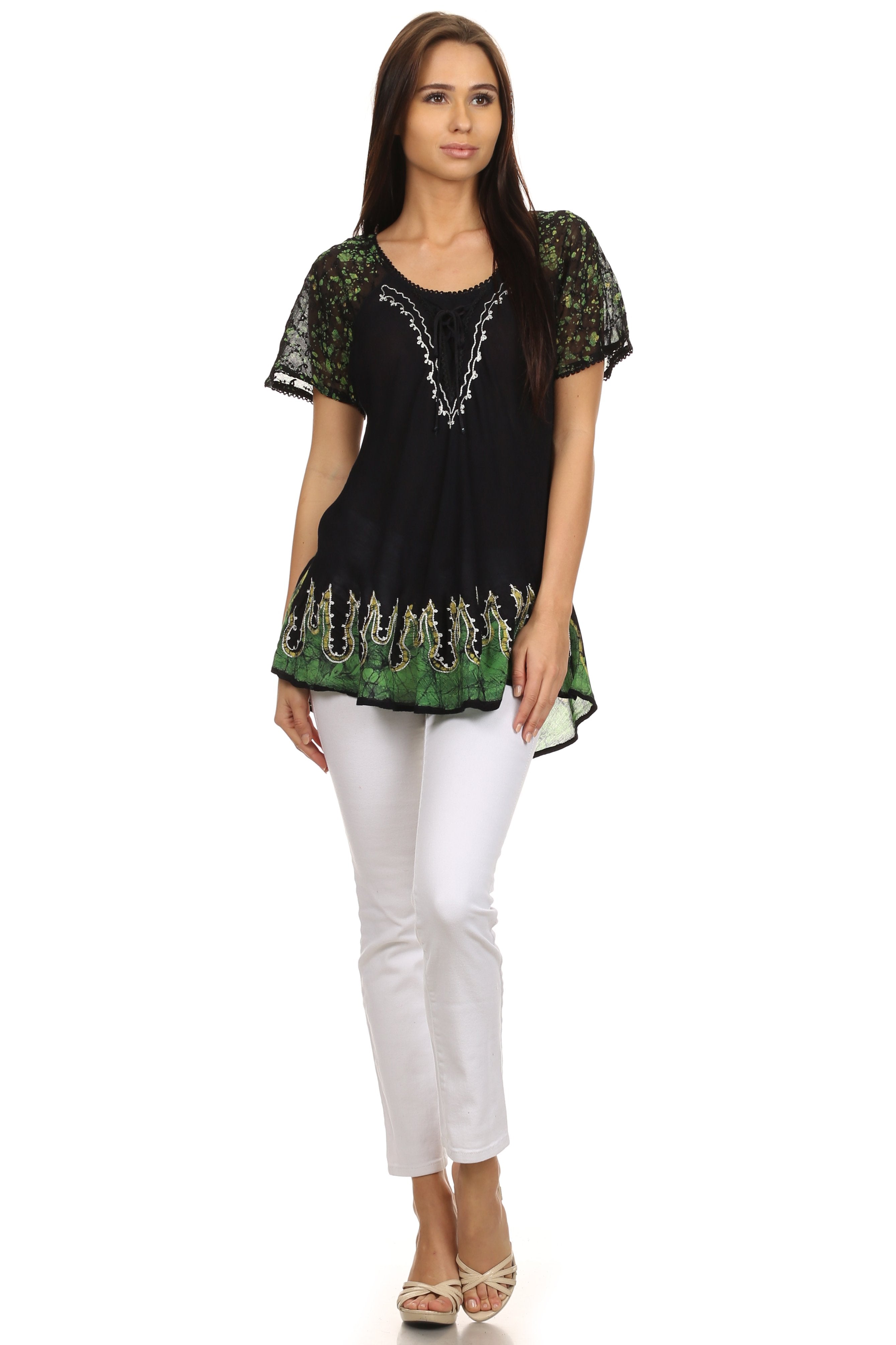 Woman wearing a black and green embroidered top with white pants on a white background
