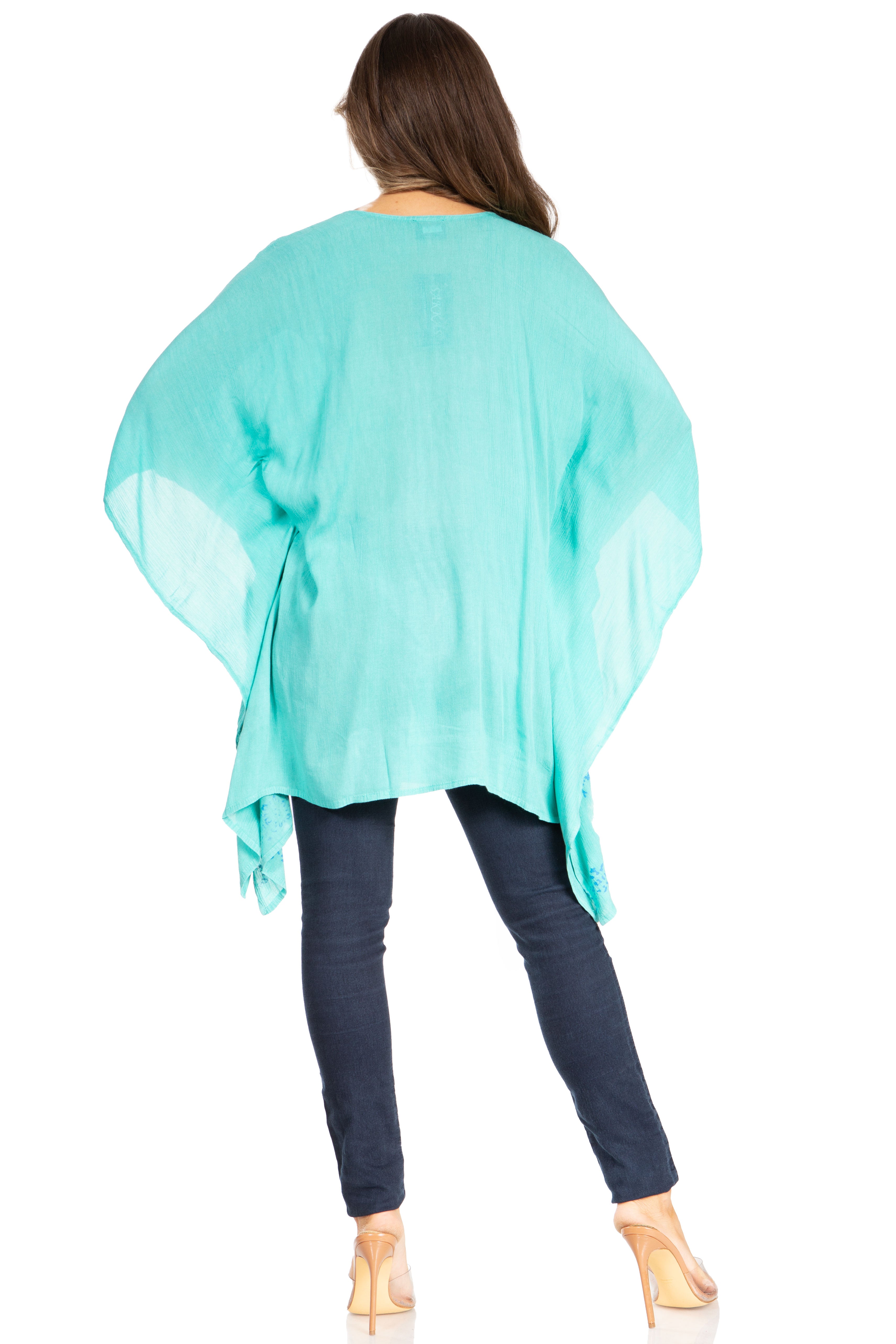 Person wearing a turquoise poncho over a dark outfit on a white background