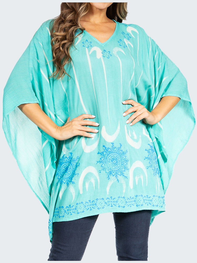 Turquoise poncho with white patterns worn by a person on a white background