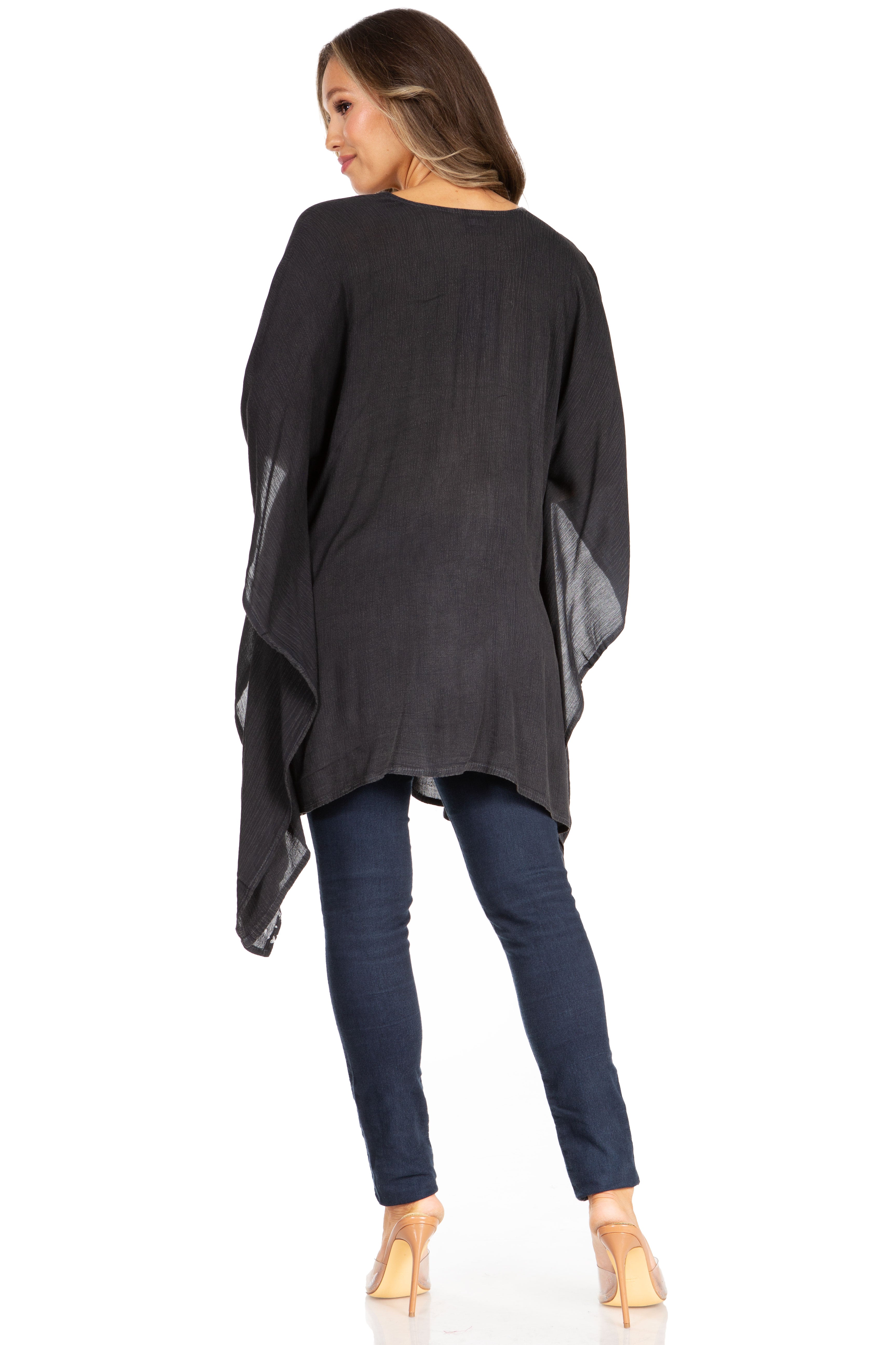 Woman wearing a dark gray poncho over a black top and blue jeans on a white background