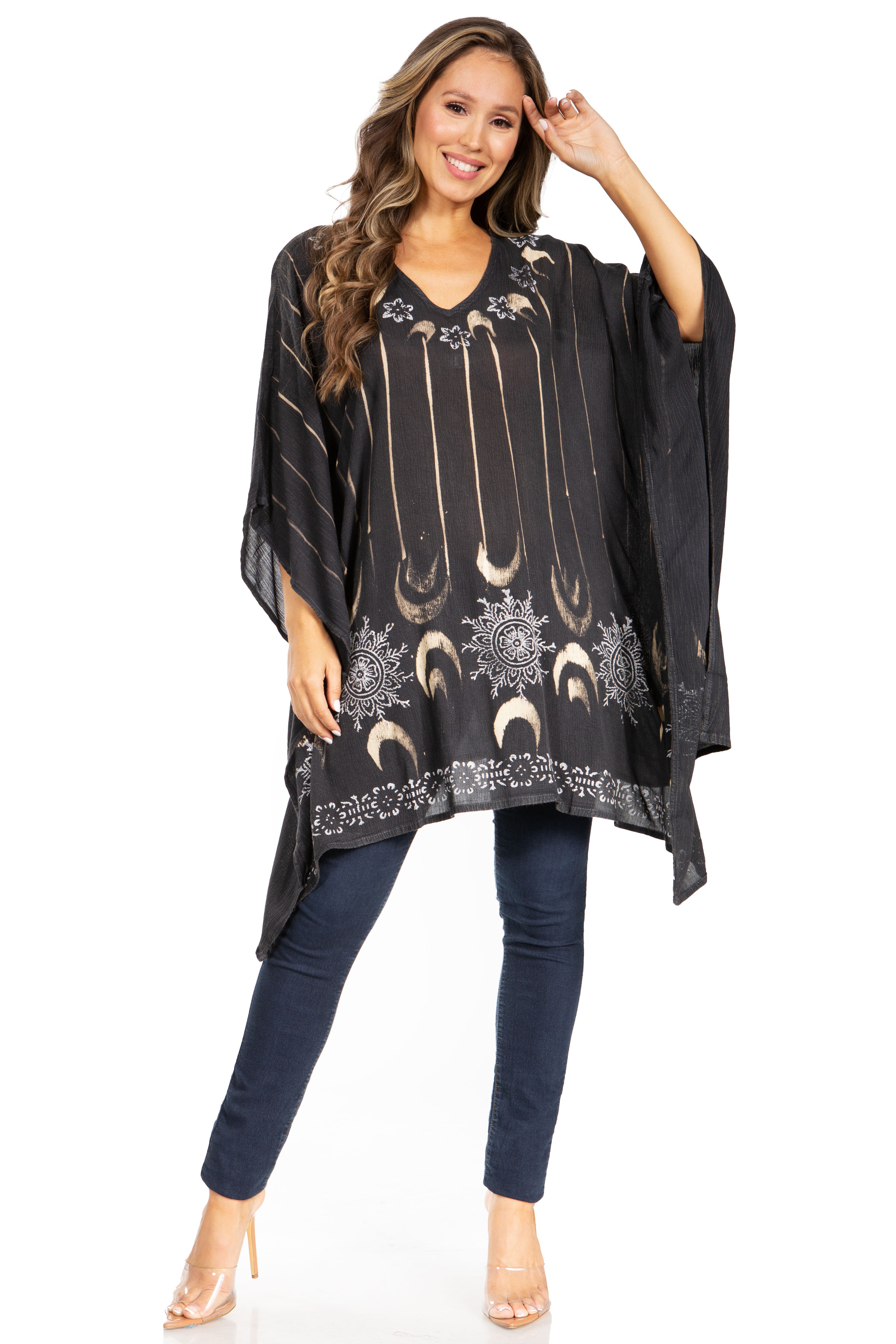 Woman wearing a black patterned poncho over a dark top and jeans on a white background