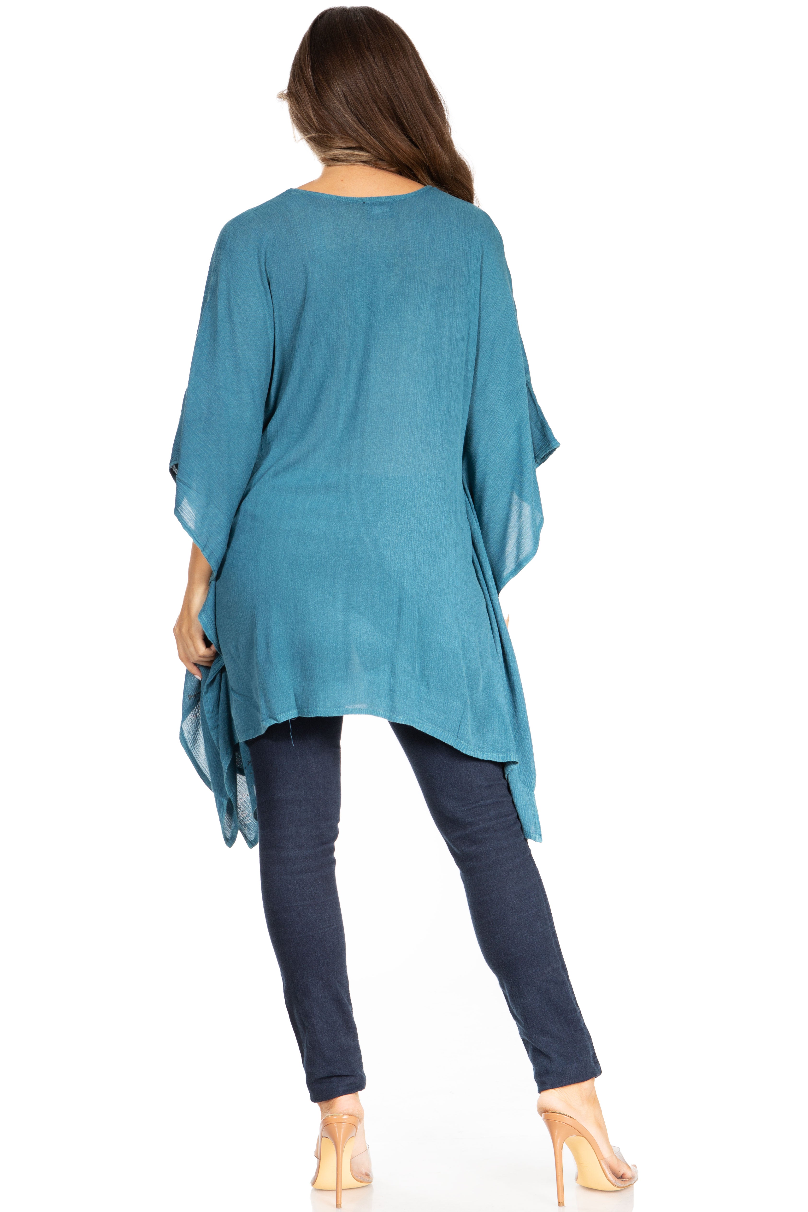 Woman wearing a teal kimono-style top and dark jeans on a white background
