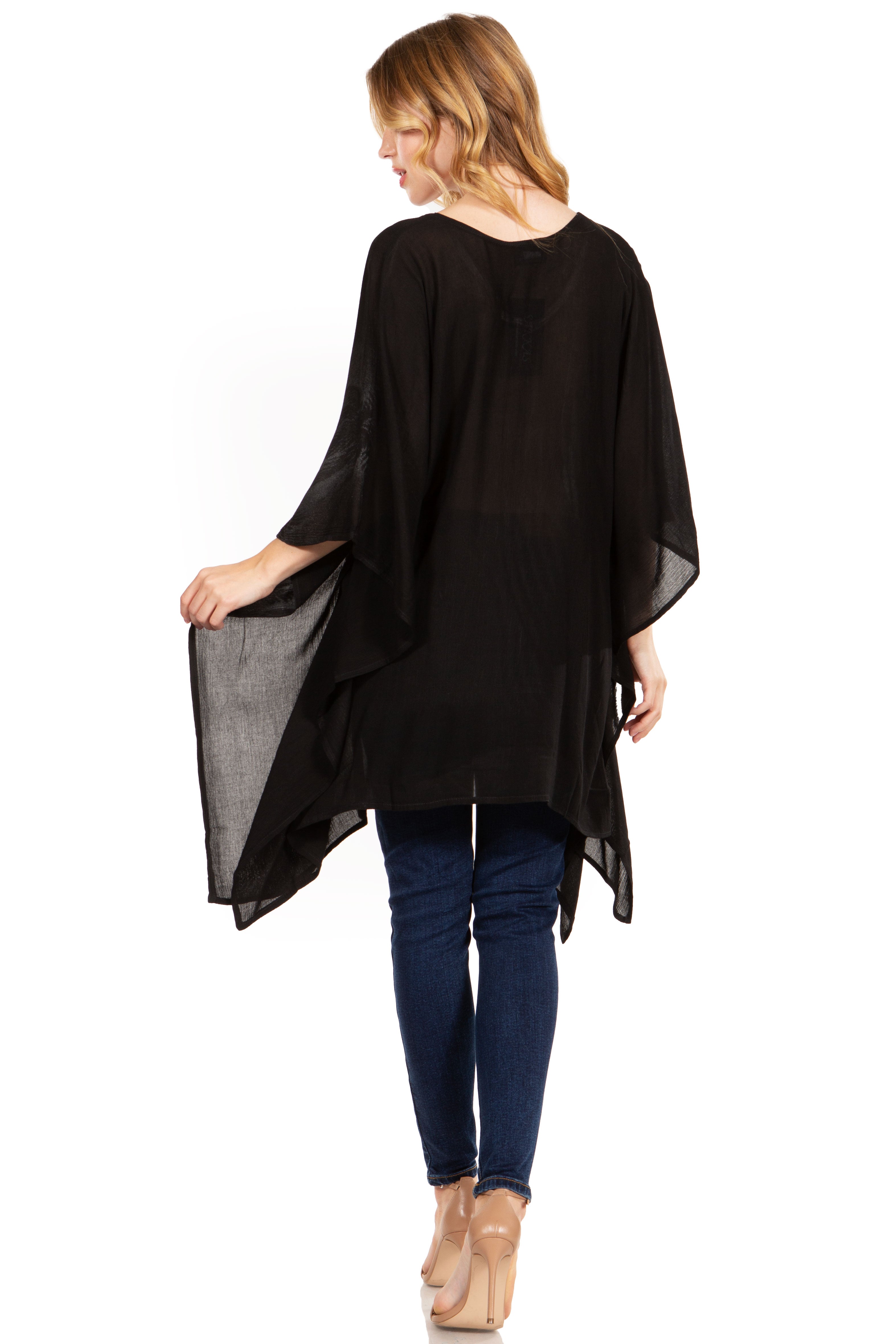 Woman wearing a black poncho over a blue top and jeans on a white background