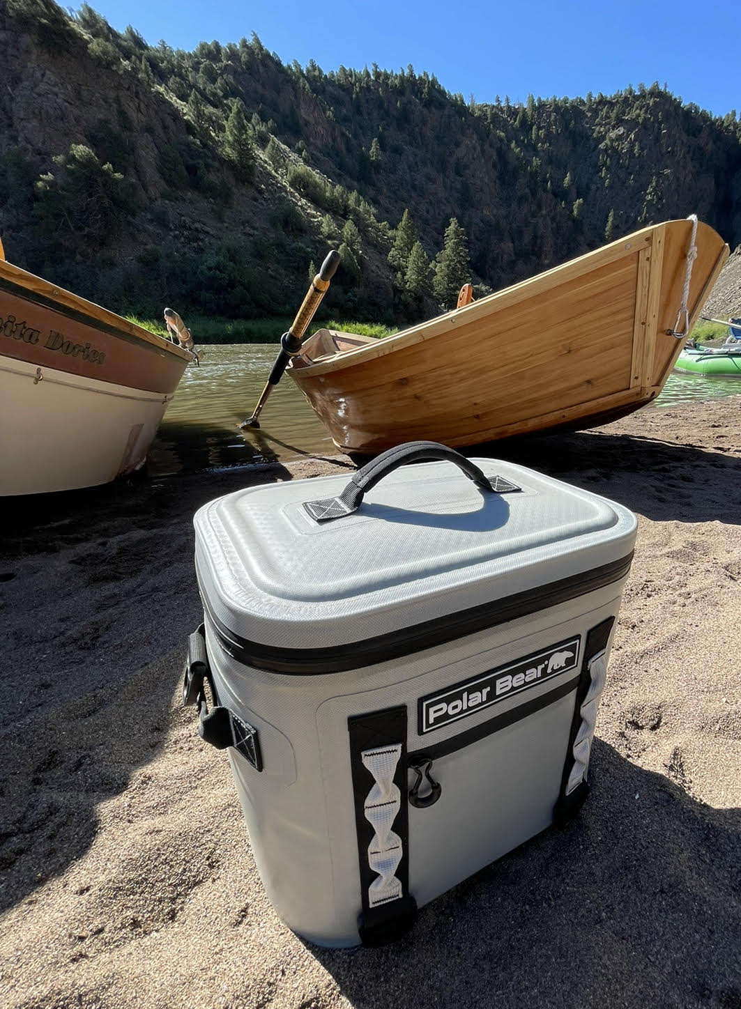 Polar Bear cooler on a sandy beach with wooden boats and a mountainous background