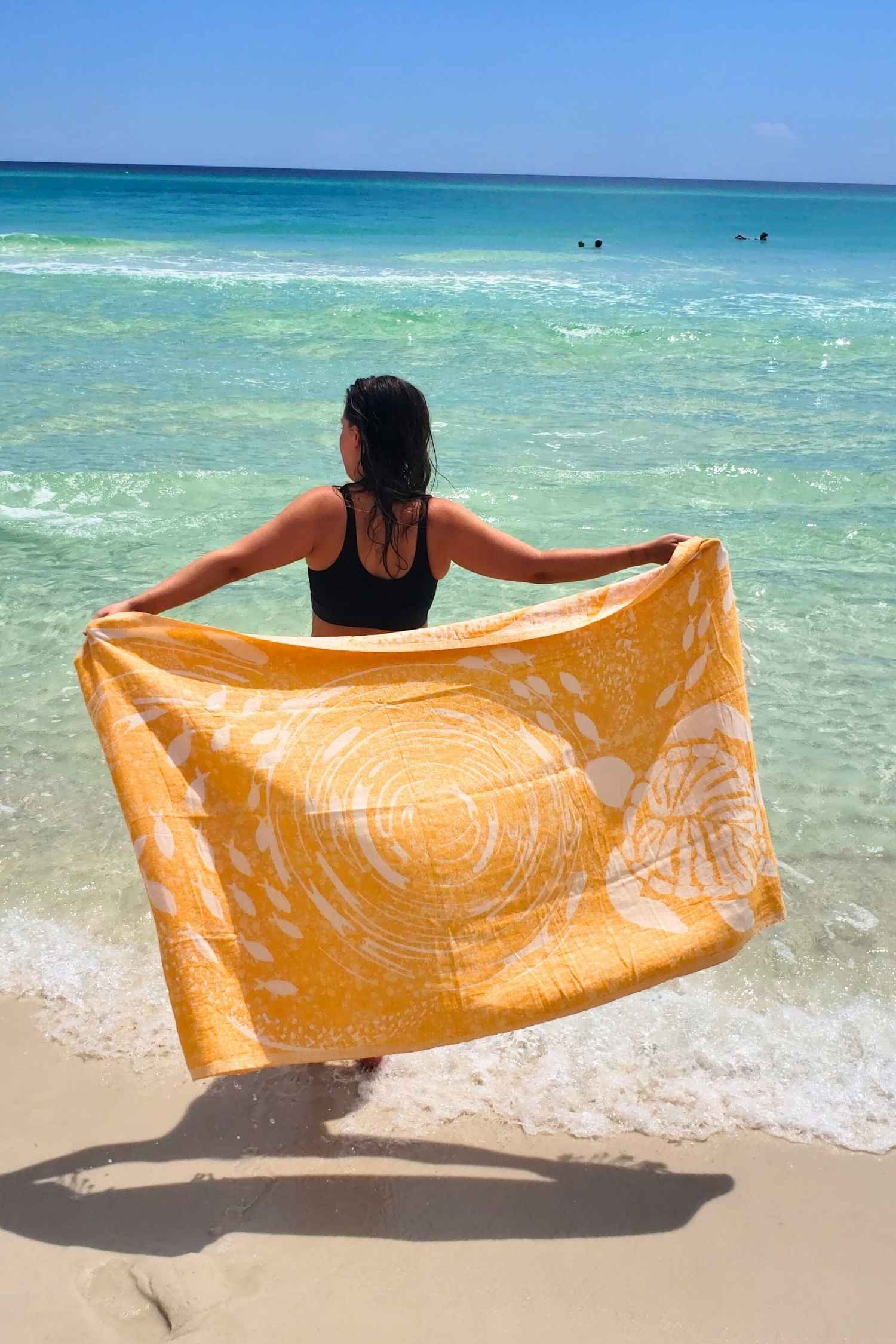 Person holding a yellow towel on a beach with clear blue water