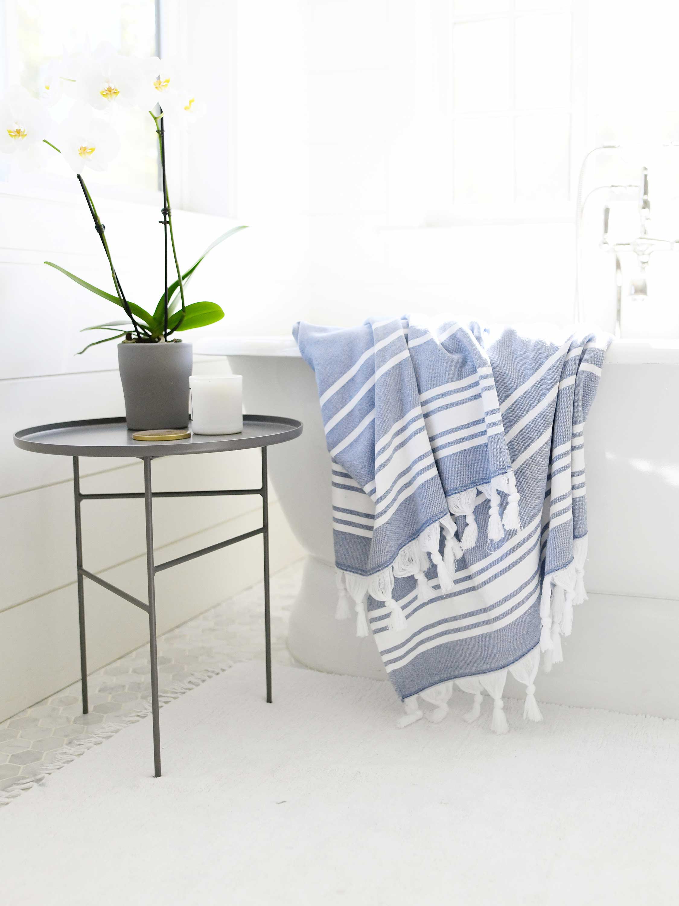 Blue and white striped towel draped over a chair next to a small round table with a plant on a white floor.