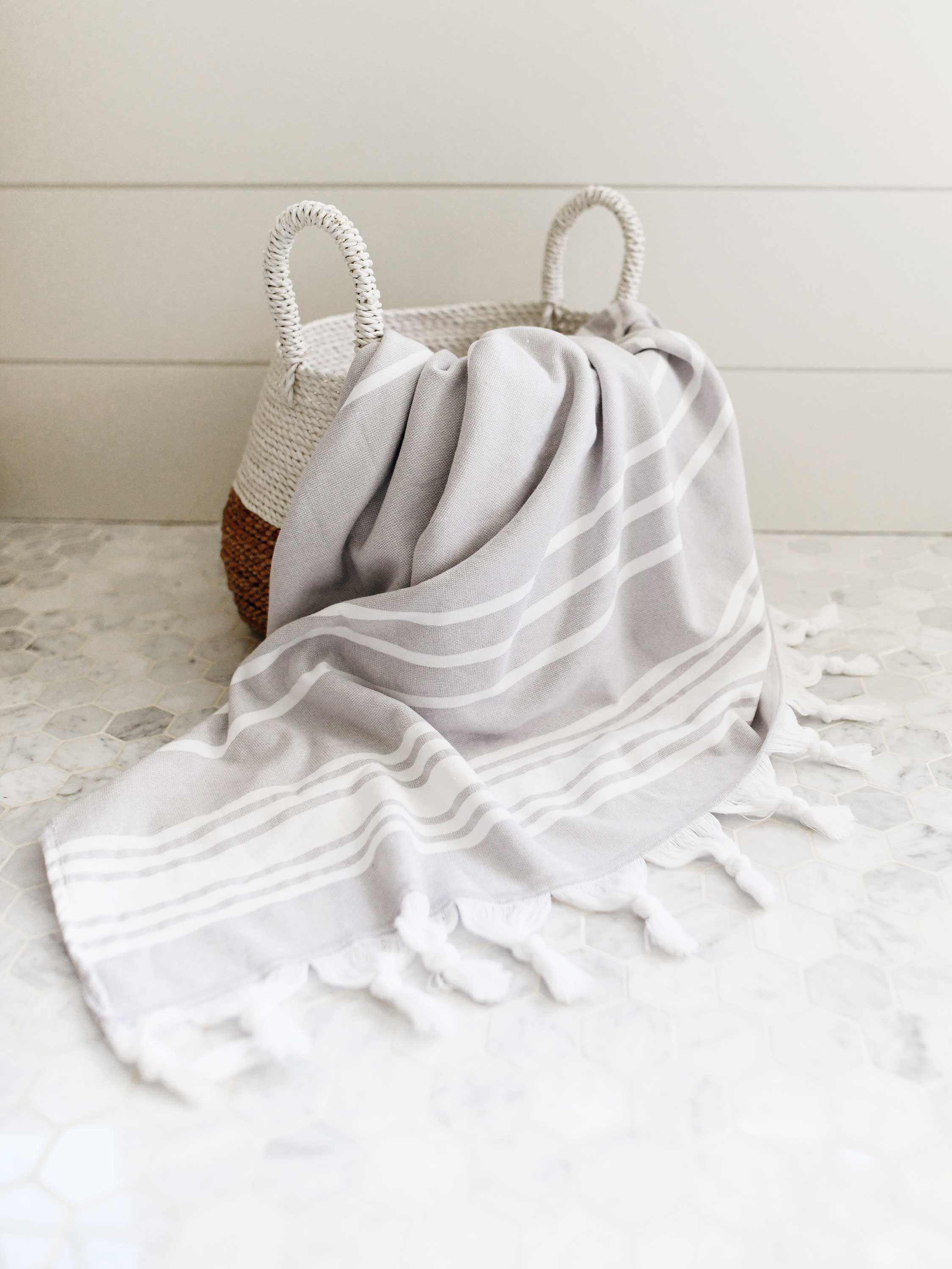 Gray striped towel draped over a woven basket on a light wooden floor.