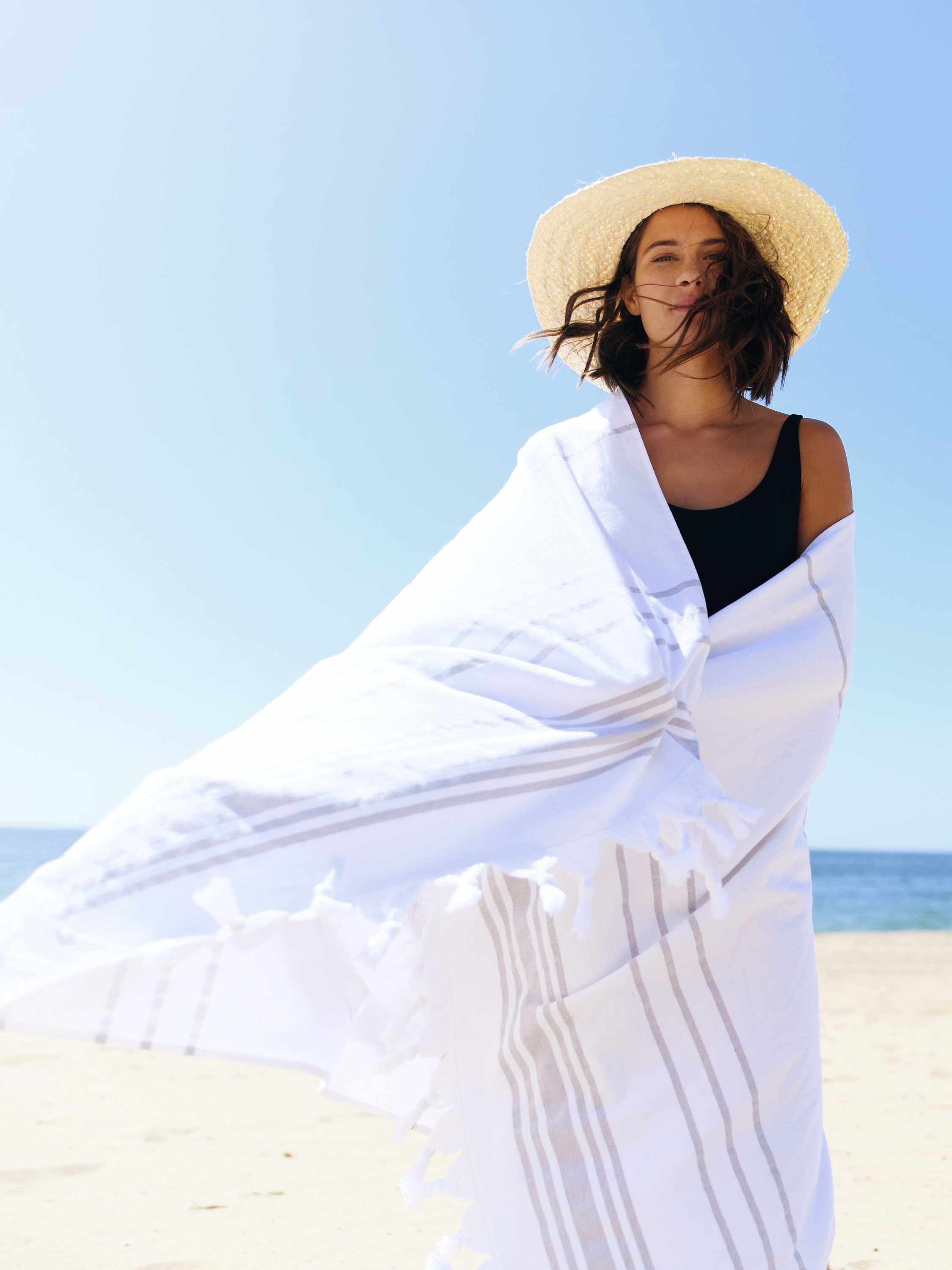 Woman wrapped in a white towel on a beach with a clear blue sky.