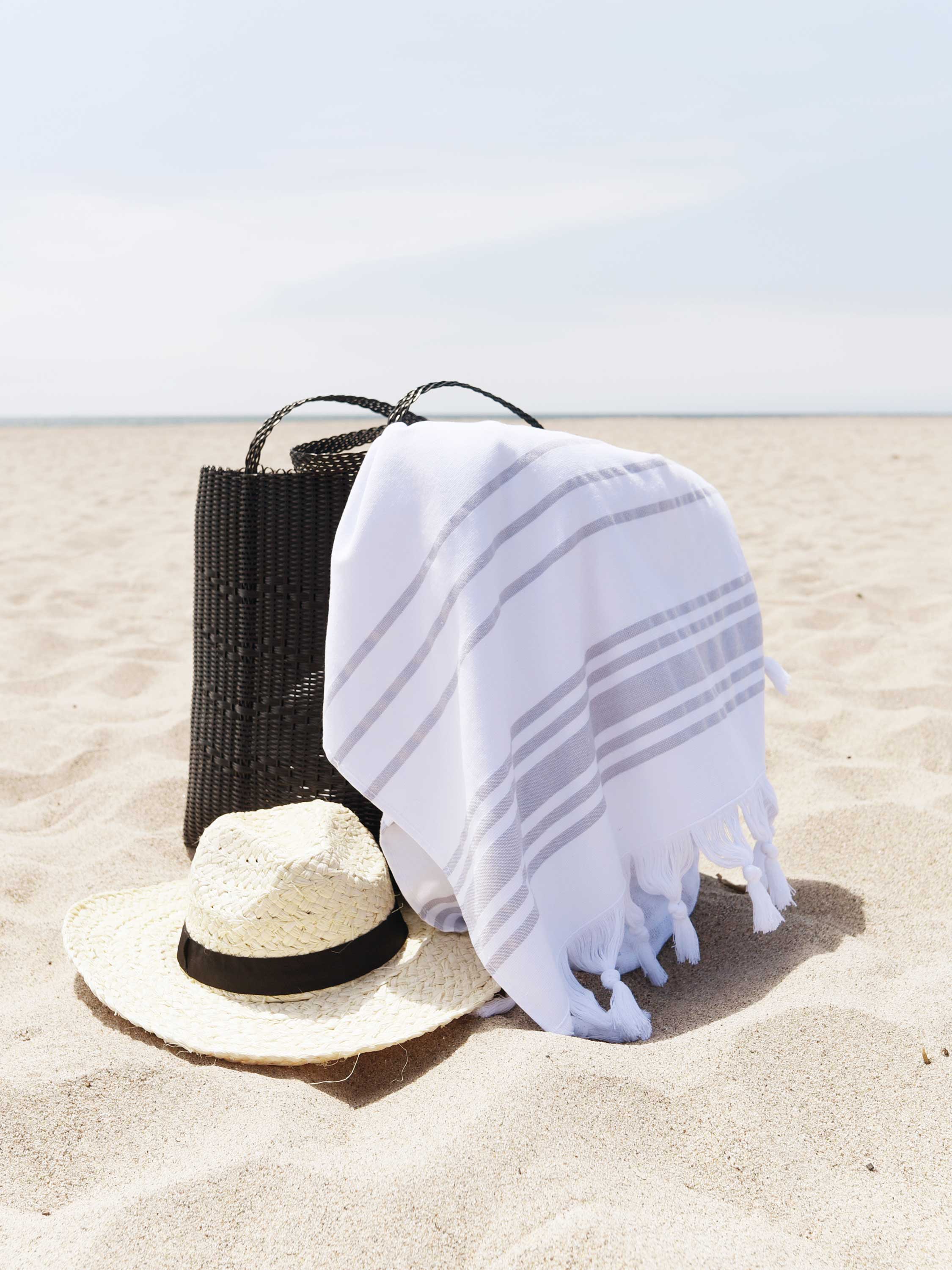 White towel with black stripes on a beach with a straw hat and black bag.