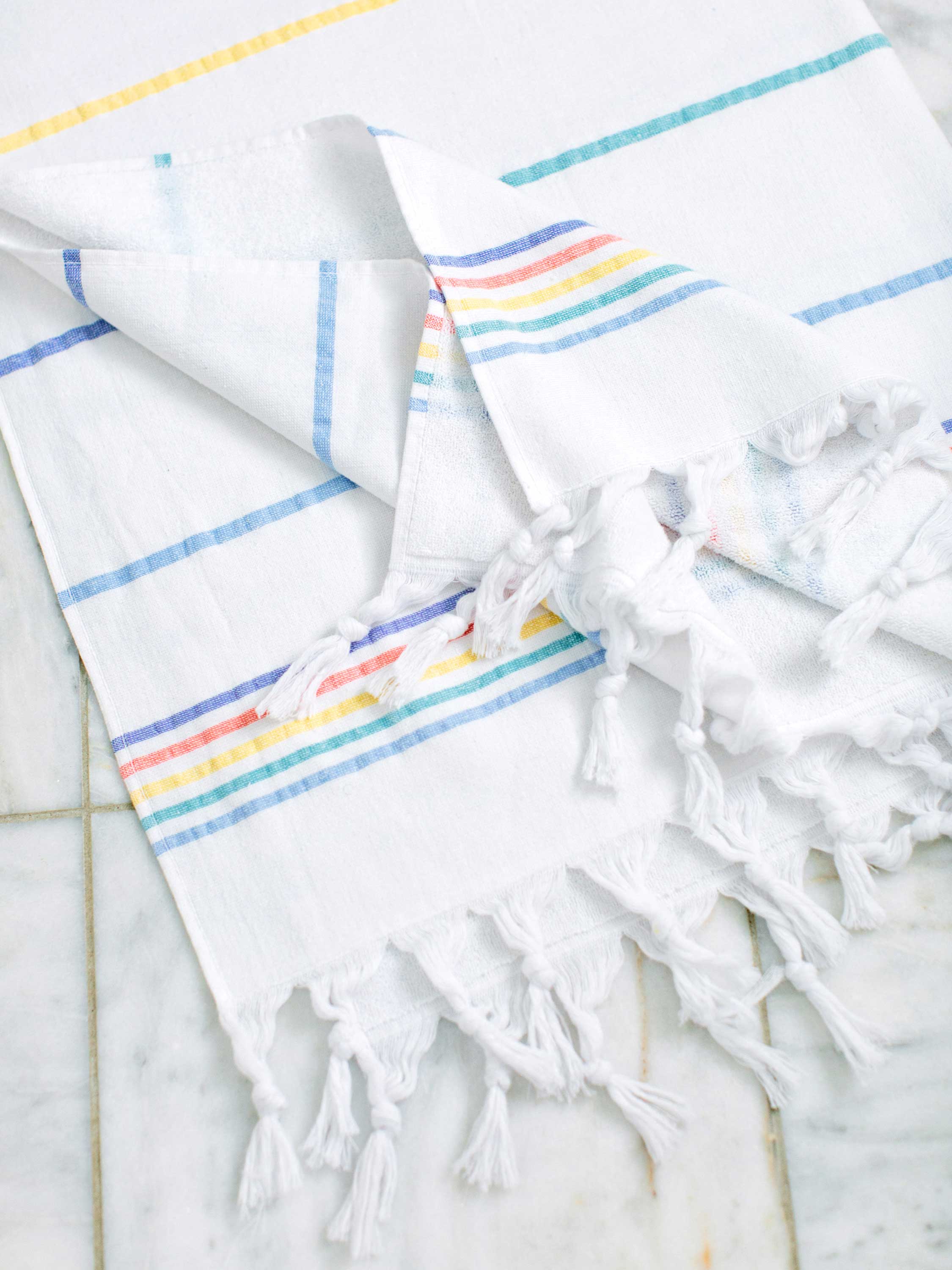 White towel with colorful stripes and tassels on a marble surface