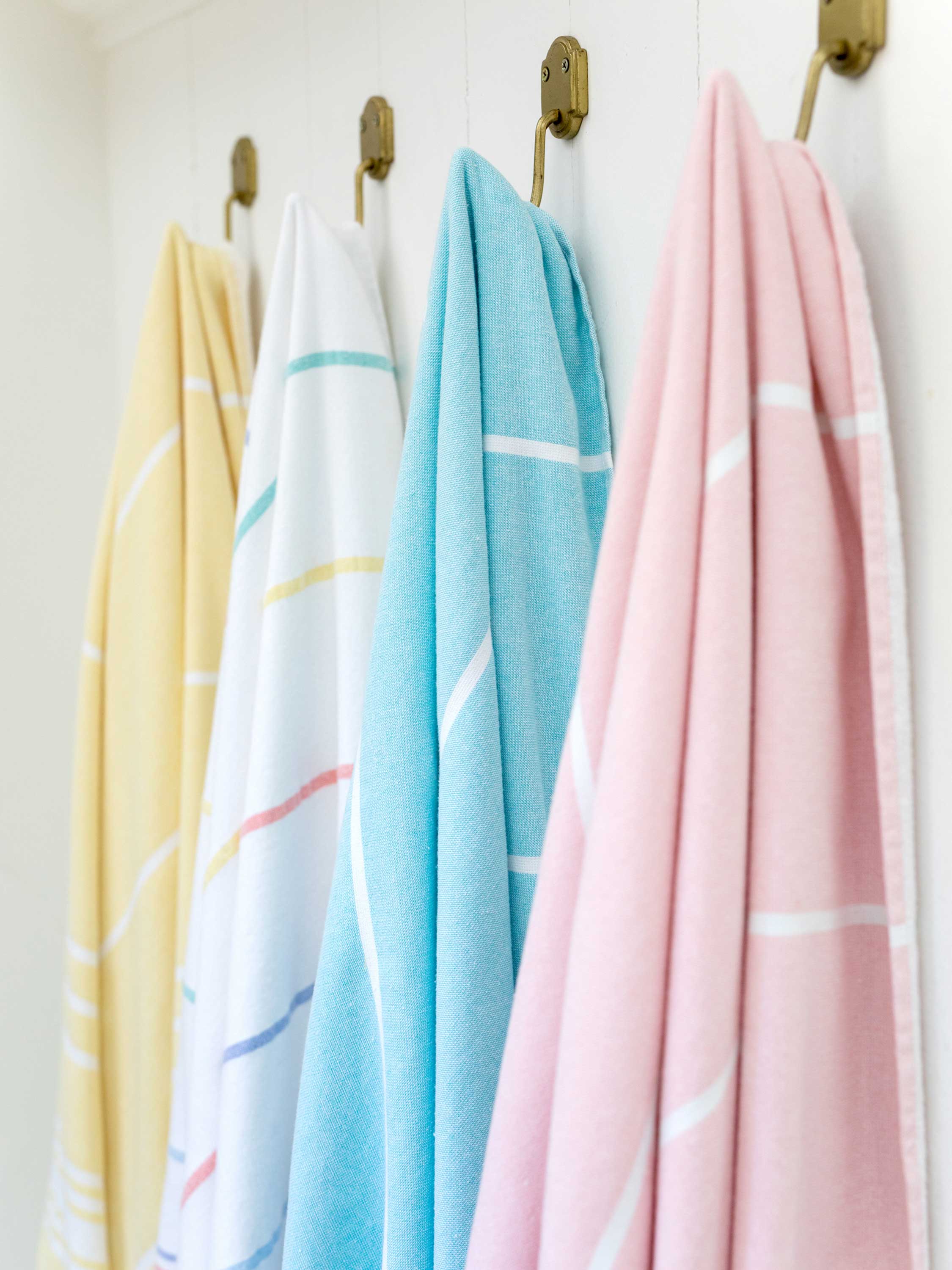 Four pastel-colored towels hanging on a rack against a white wall.