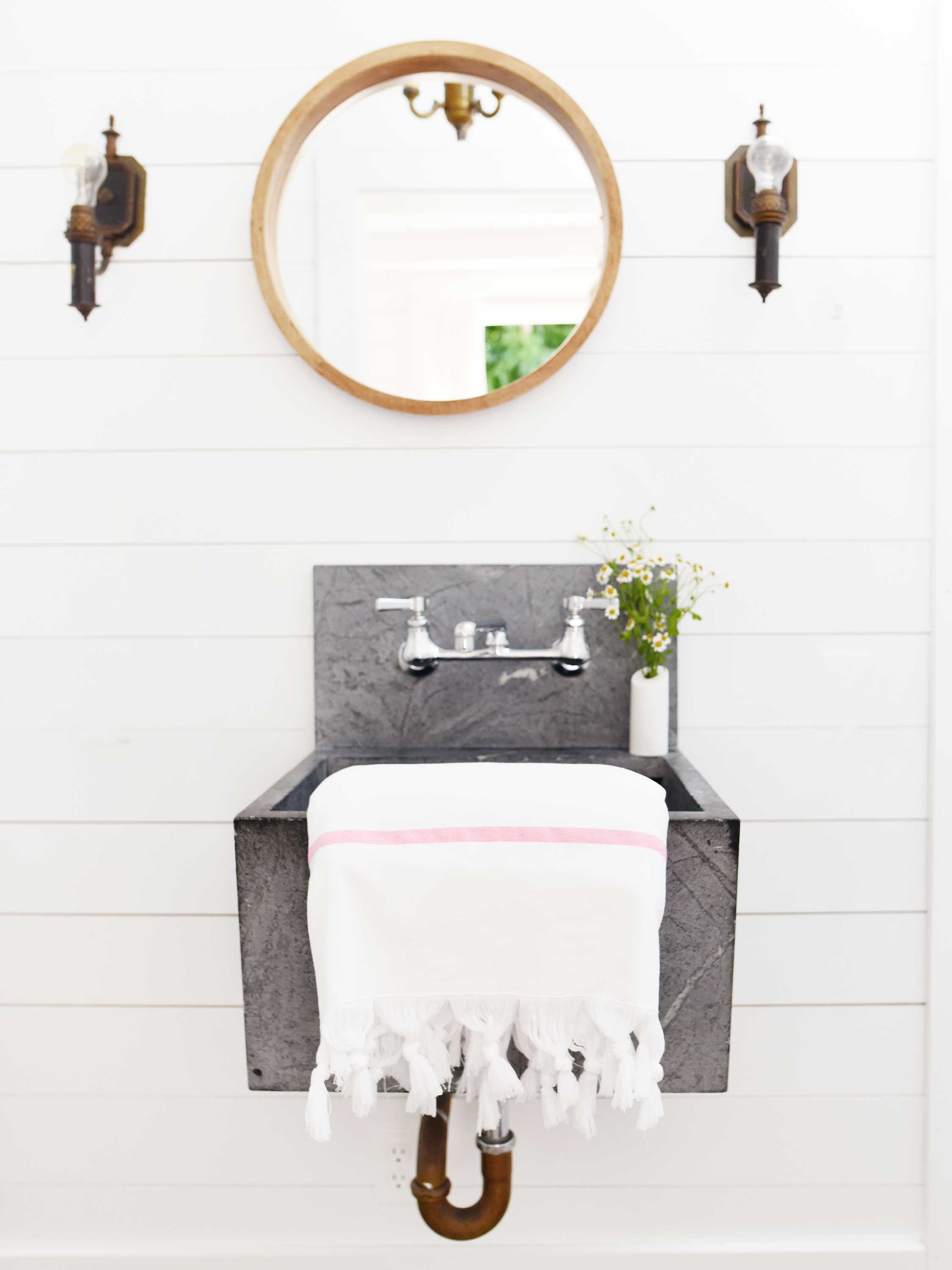 Bathroom with gray sink, white towel, and round mirror on white wall.