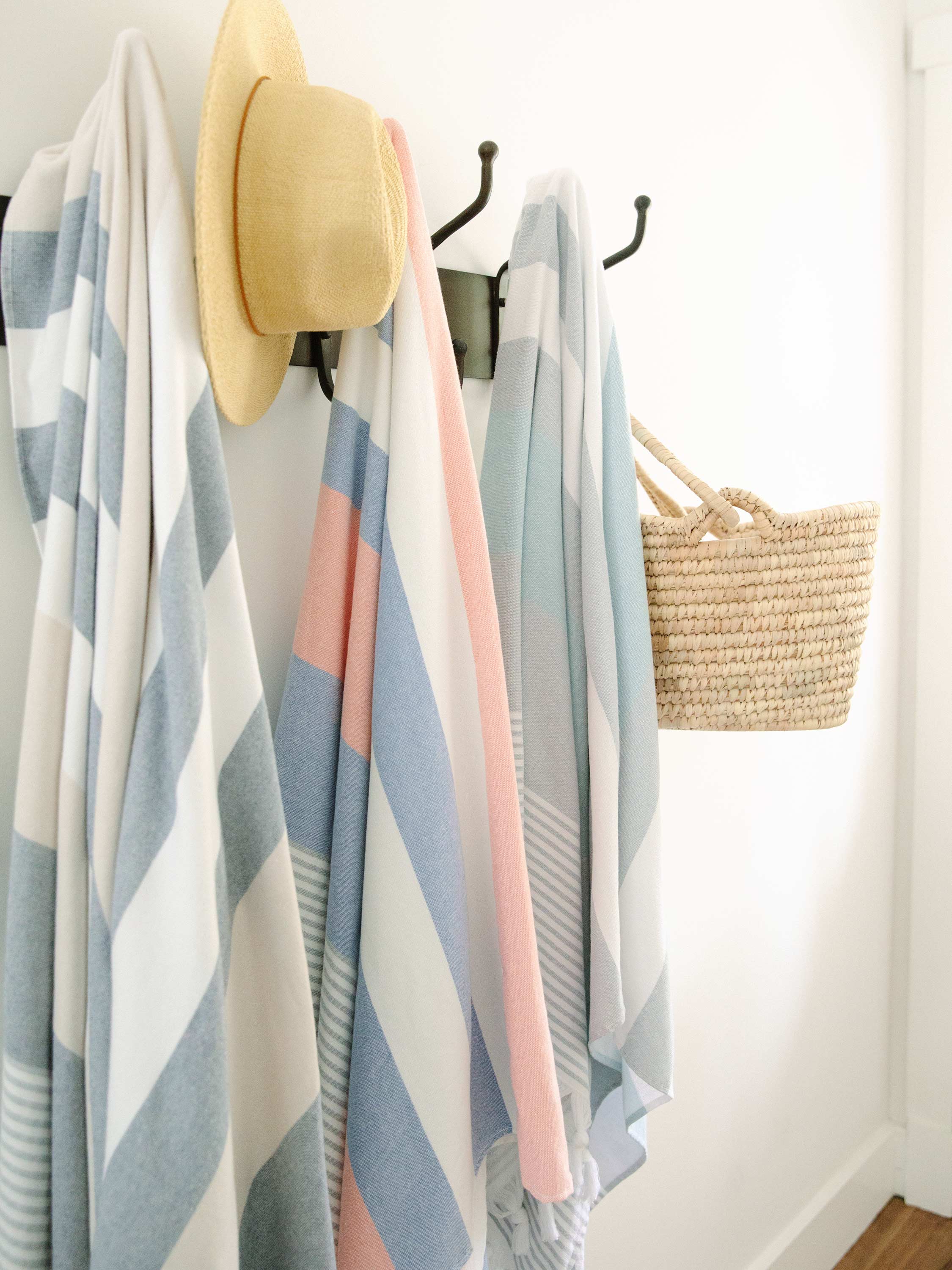 Striped towel with a hat and basket hanging on hooks against a white wall.