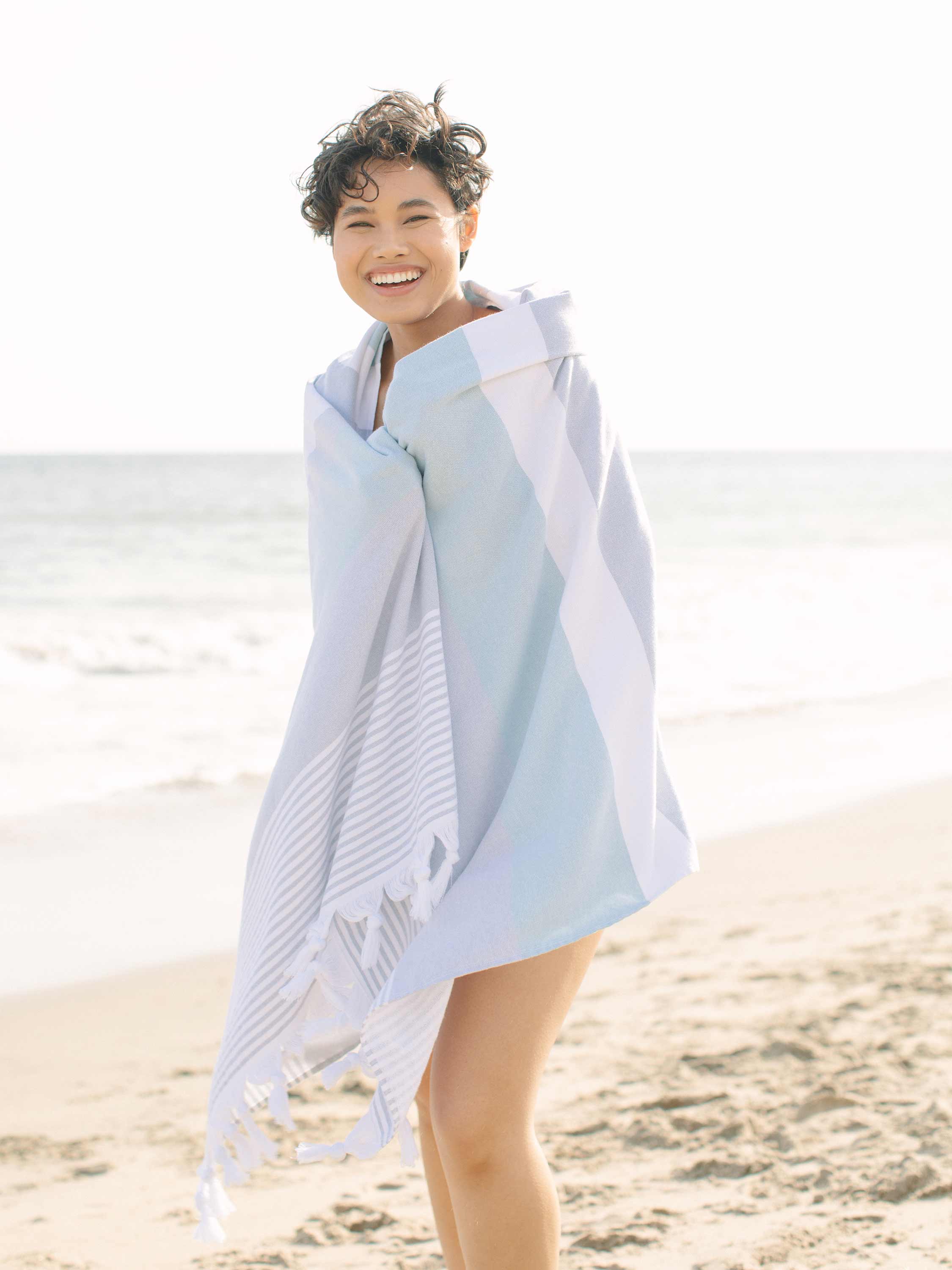 Person wrapped in a light blue towel on a beach