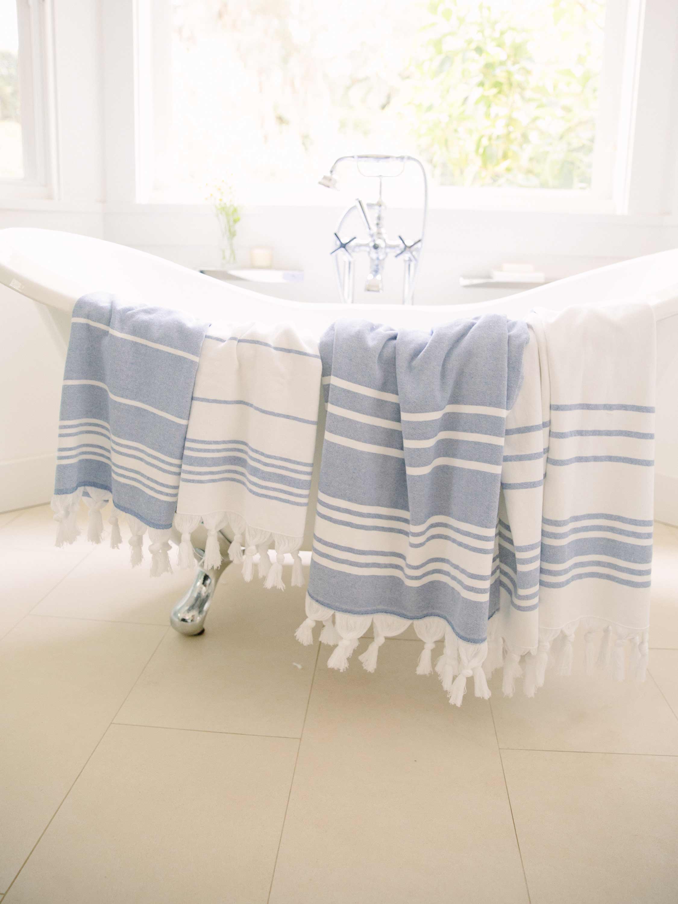 Blue and white striped towel draped over a bathtub in a bright bathroom.