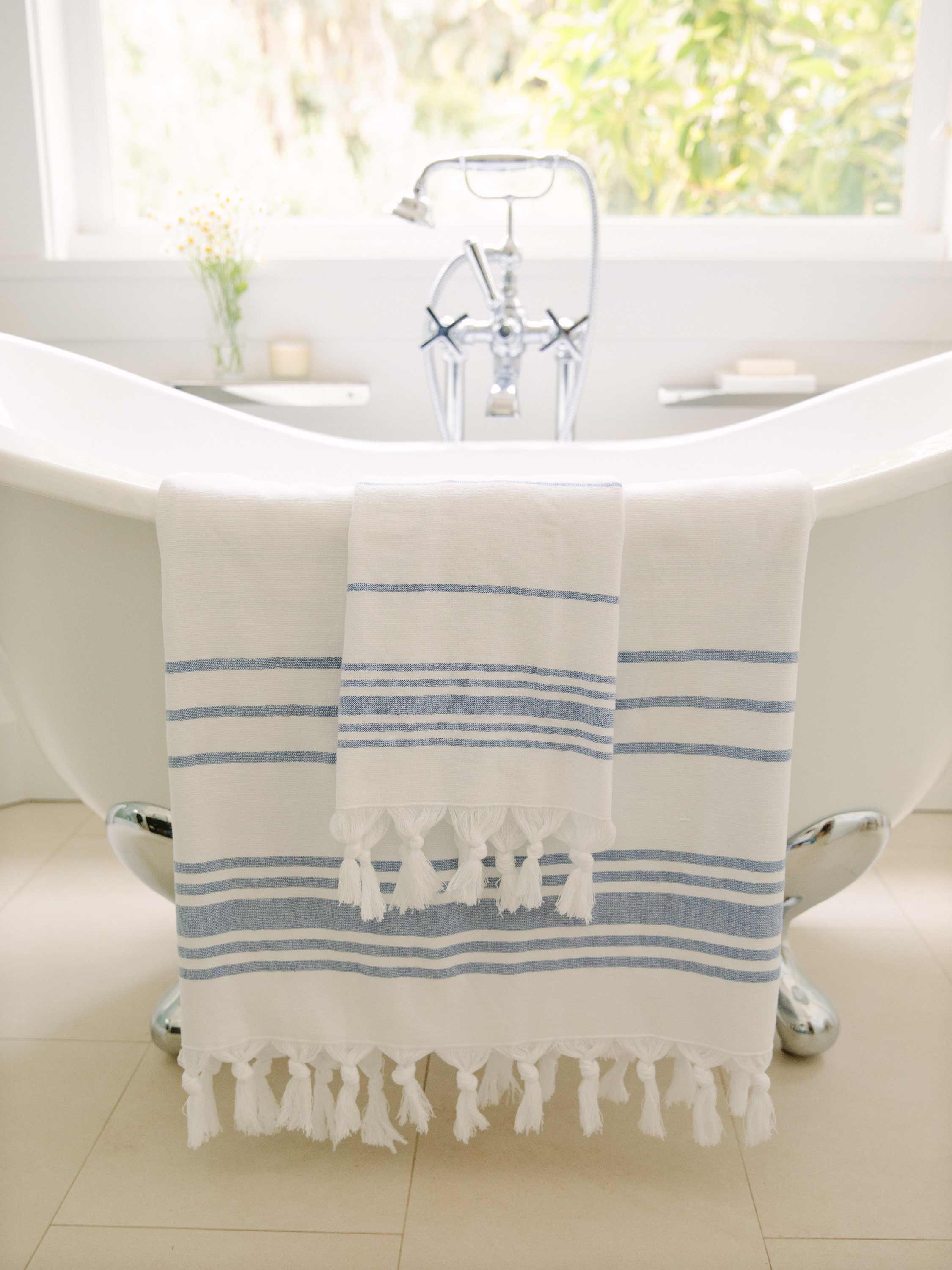 White towel with blue stripes and tassels draped over a white bathtub in a bathroom.