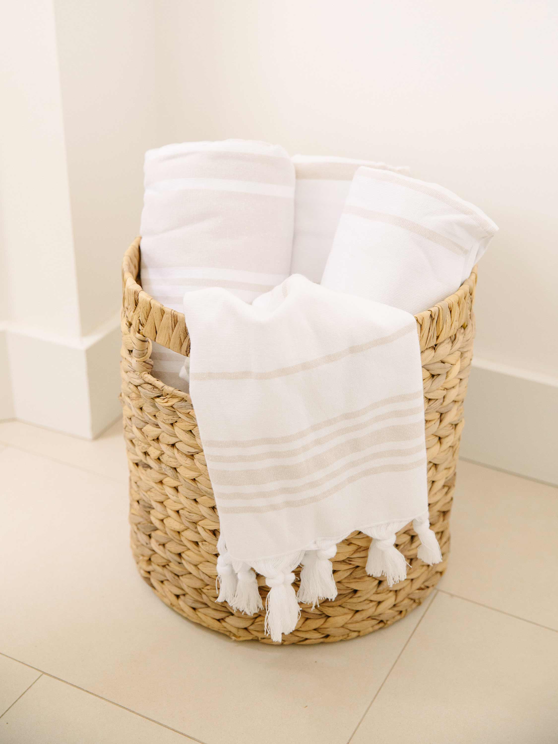 Wicker laundry basket filled with white towels on a light wooden floor.