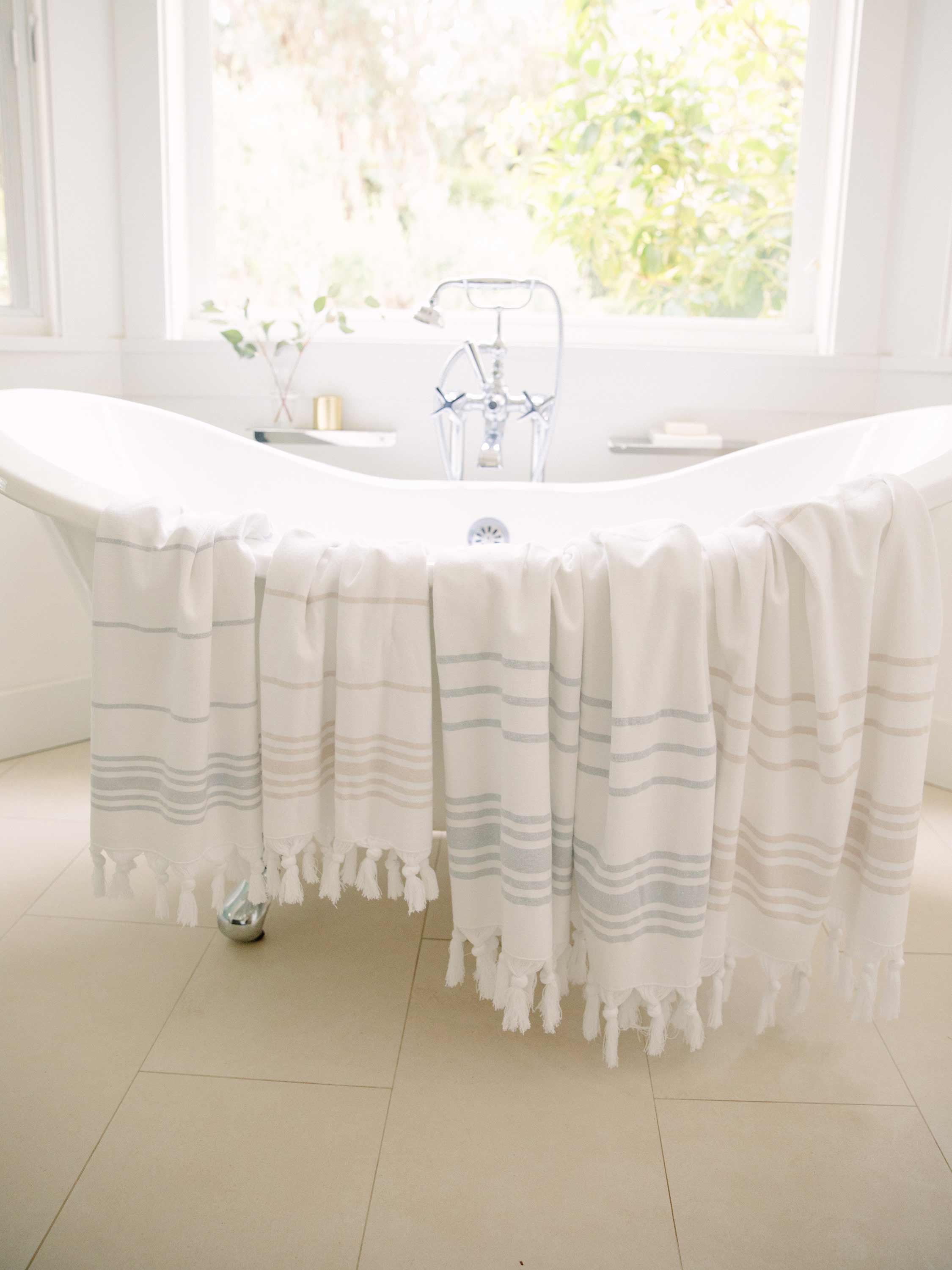 White bath towel with gray stripes draped over a bathtub in a bright bathroom.