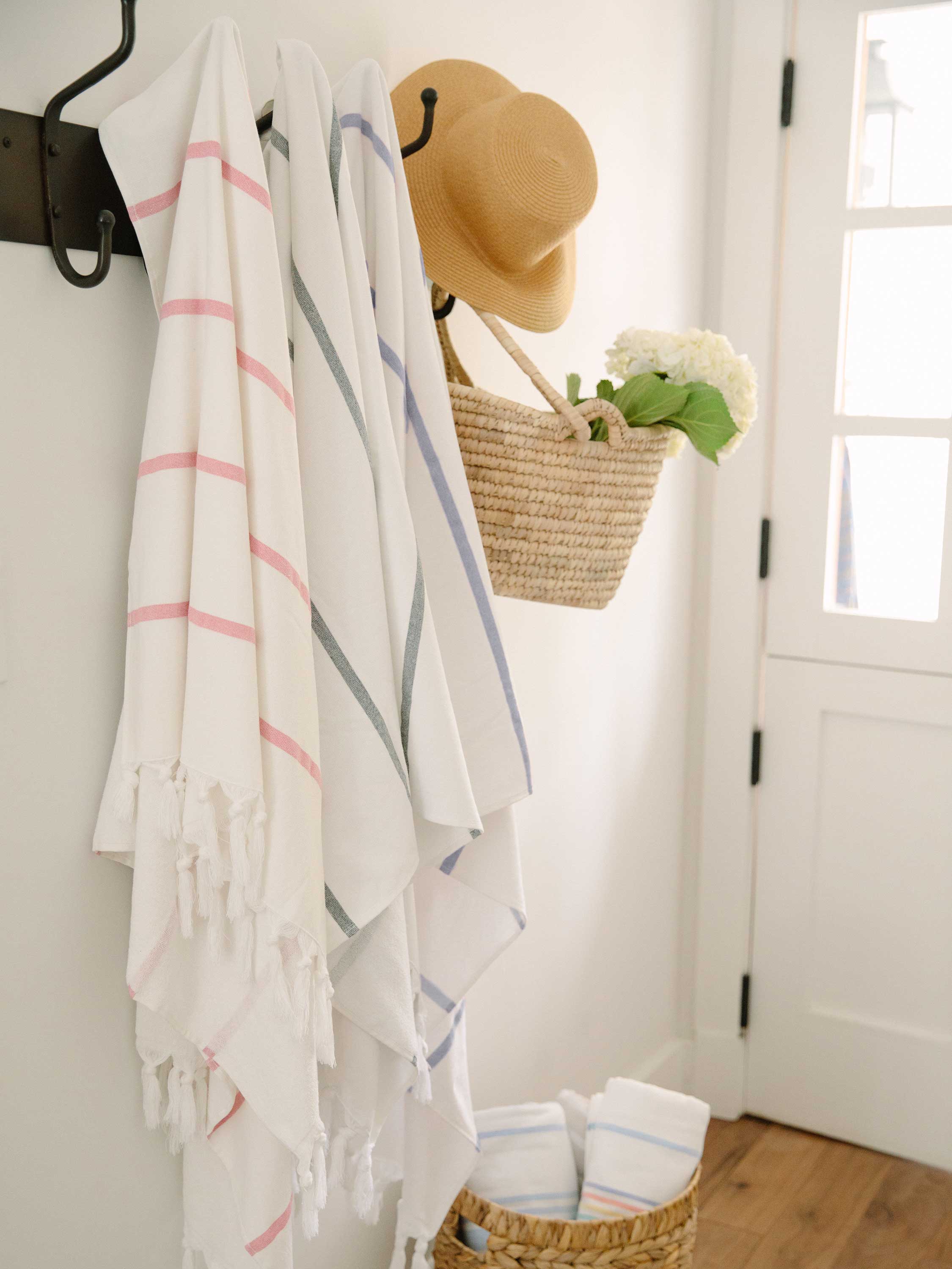 Striped towels hanging on a rack with a hat and basket in a room.