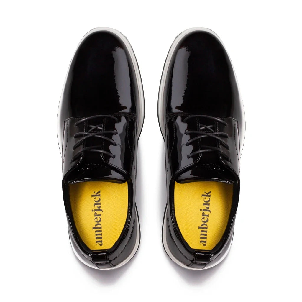 Black patent leather shoes with yellow soles on a white background