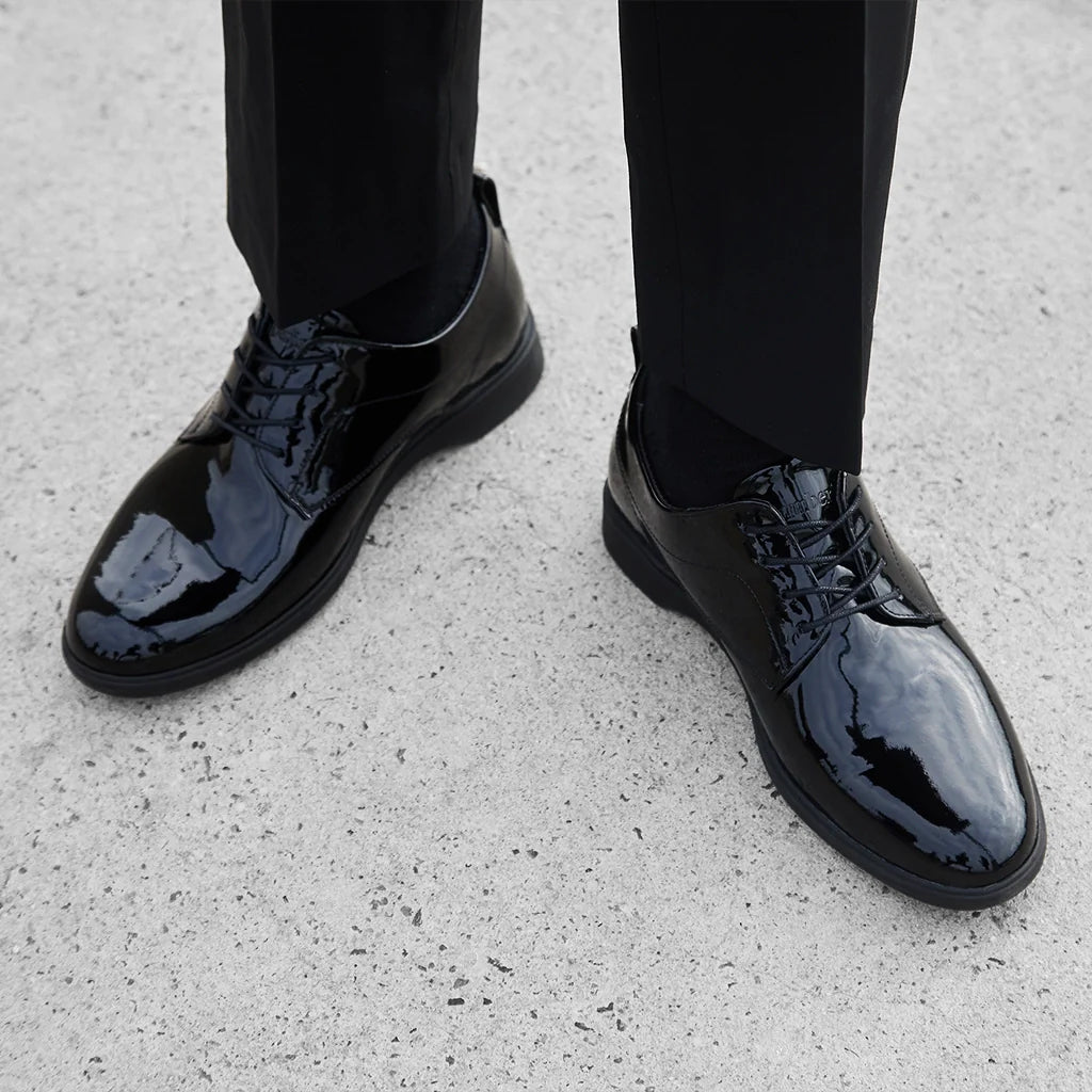 Black patent leather shoes worn with black pants on a light gray surface