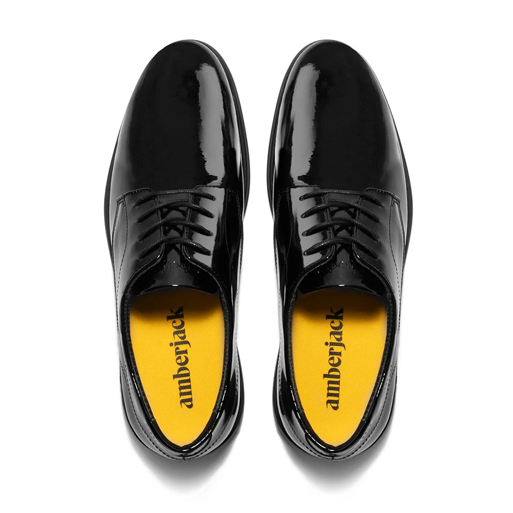 Black patent leather shoes with yellow soles on a white background