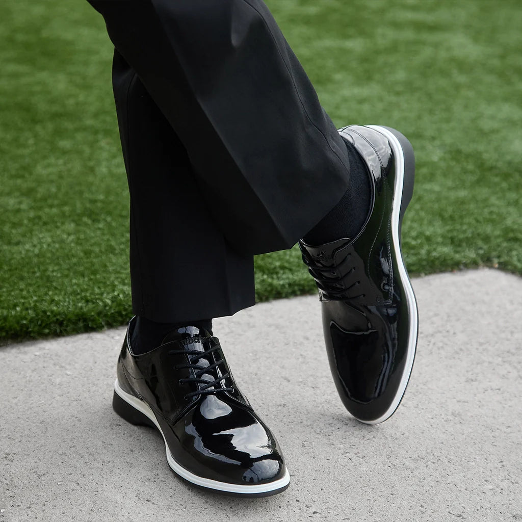 Black patent leather shoes worn with black pants on a concrete surface with grass in the background