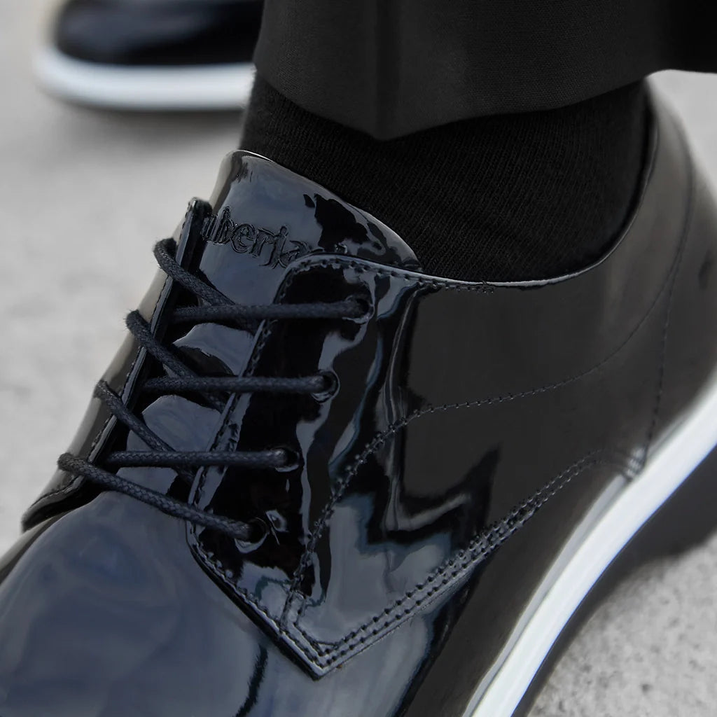 Black patent leather shoe with brand name on a concrete surface