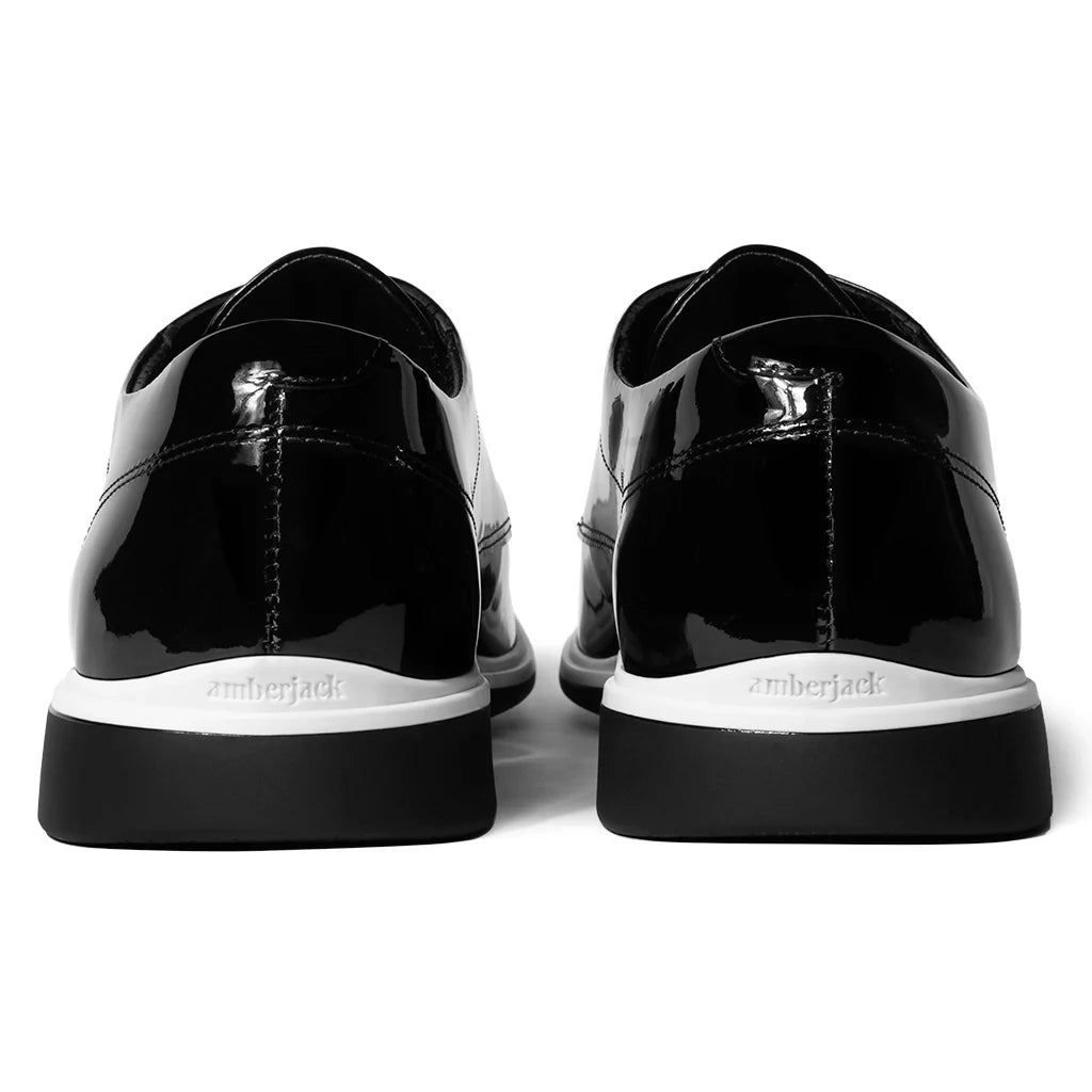 Black patent leather shoes with white soles on a white background