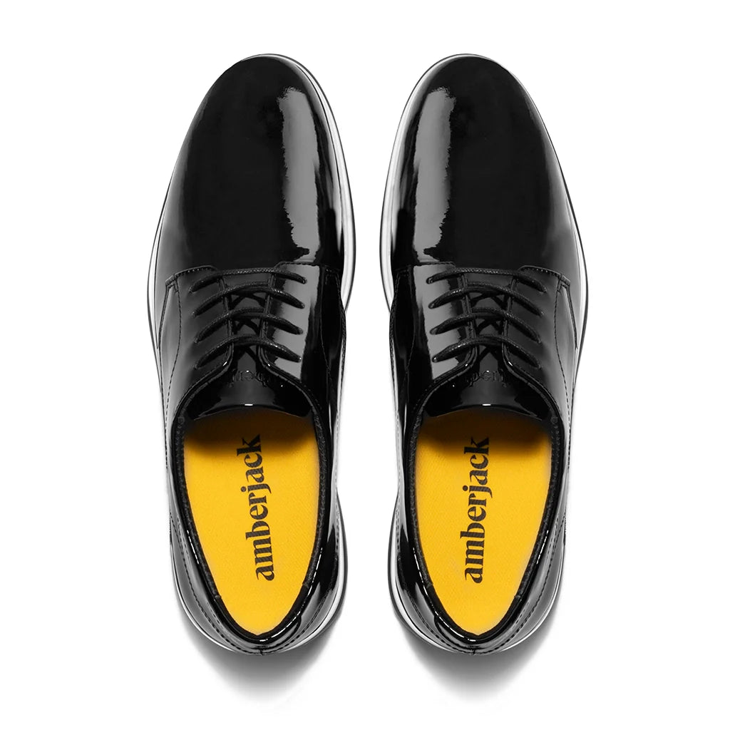 Black patent leather shoes with yellow soles on a white background