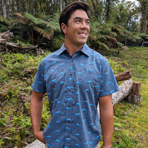 Man wearing a blue patterned shirt standing in a forest setting