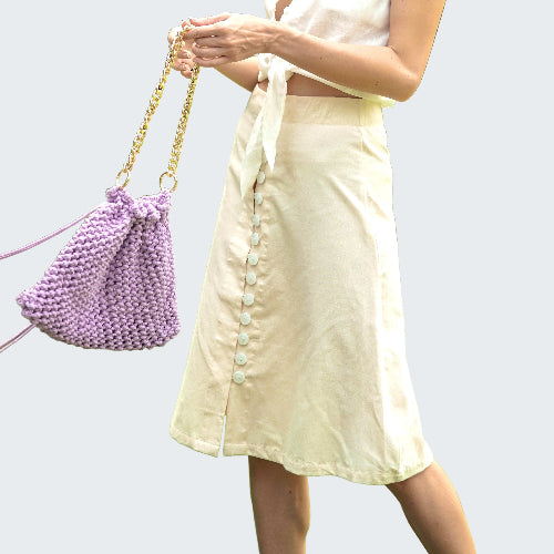 Person holding a purple beaded handbag with a blurred green outdoor background