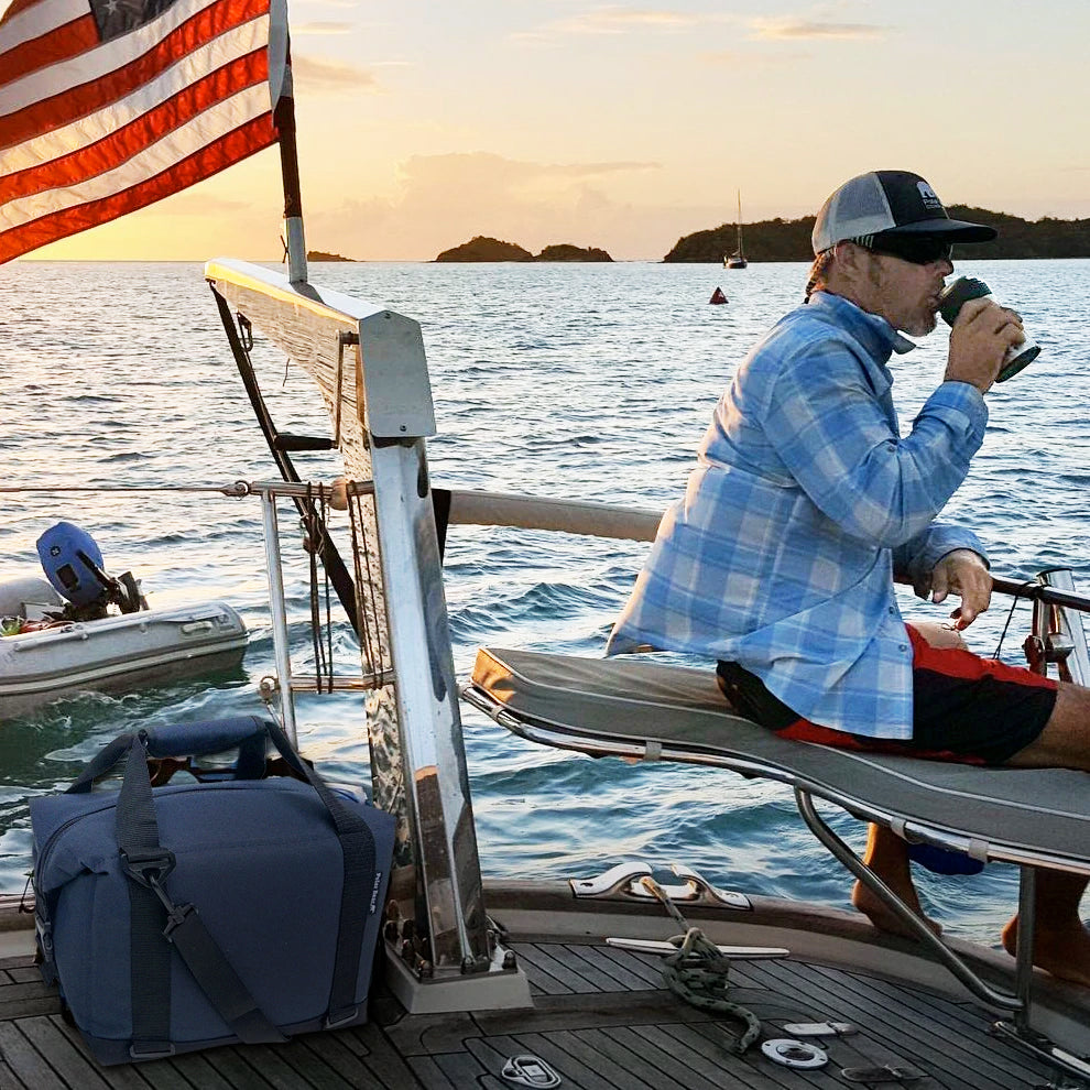 Person on a boat with an American flag, drinking from a cup, sunset over water
