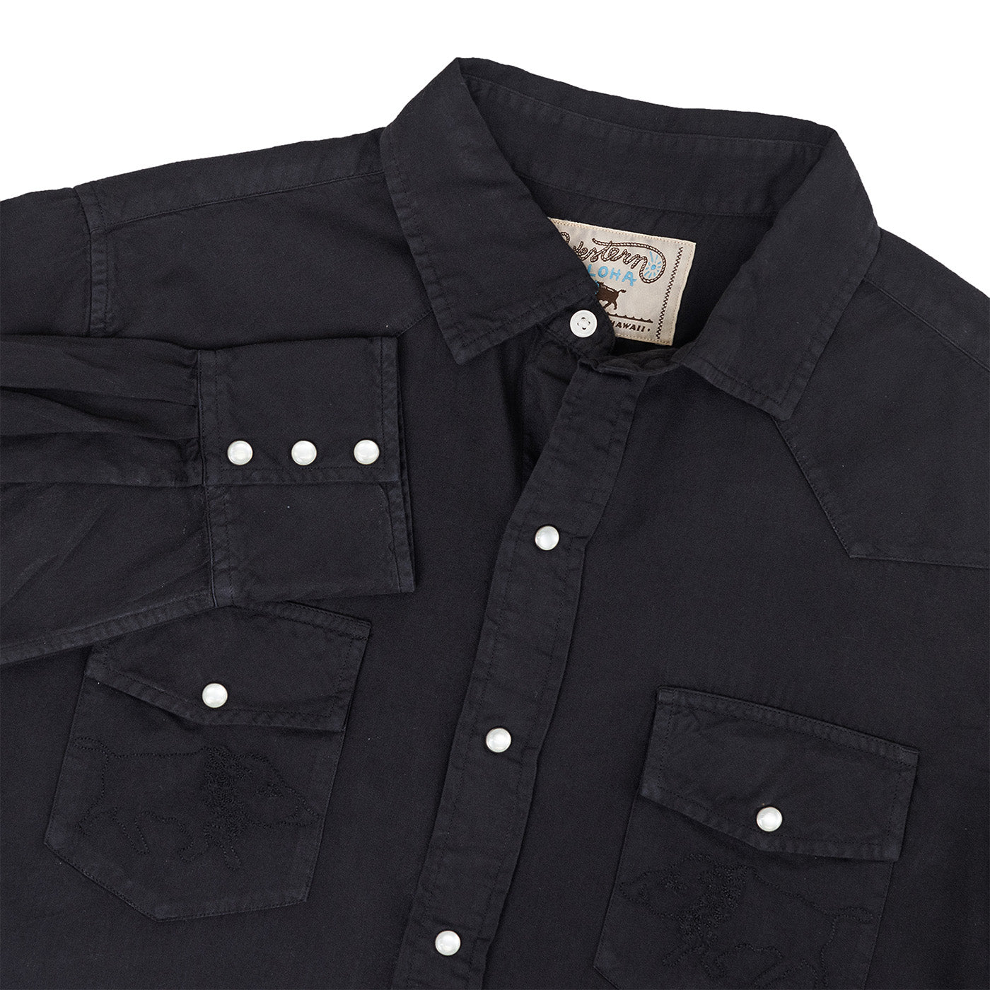 Close-up of a black shirt with button details and a visible brand label on a white background