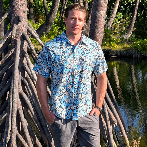 Man in a blue floral shirt standing among mangrove roots with water and greenery in the background