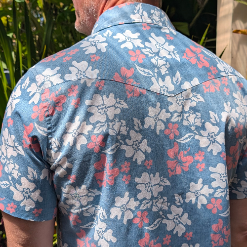 Person wearing a blue floral shirt with red and white flowers against a natural background