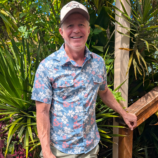 Man wearing a floral shirt and cap standing among green plants