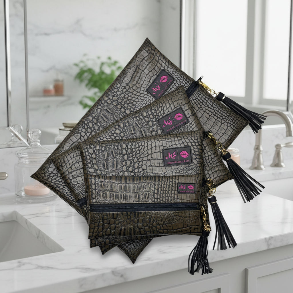 Set of gray crocodile-textured pouches with black tassels and pink logo tags on a white background