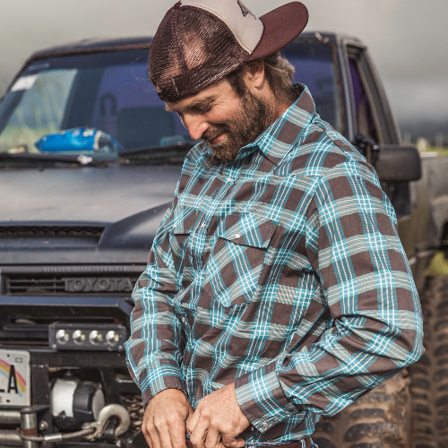 Man wearing a plaid shirt and cap standing in front of a Toyota truck