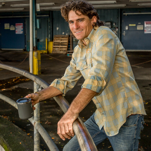 Man in plaid shirt holding a cup, standing in an industrial setting