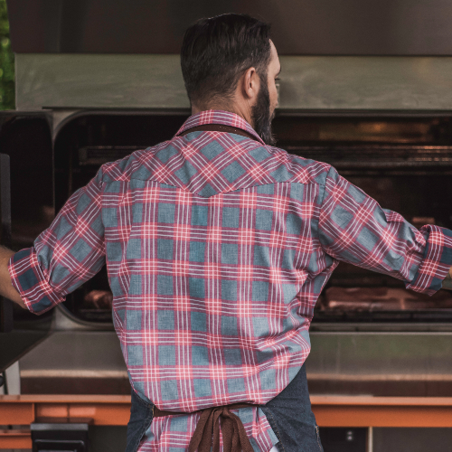 Man wearing a plaid shirt standing in front of an outdoor grill
