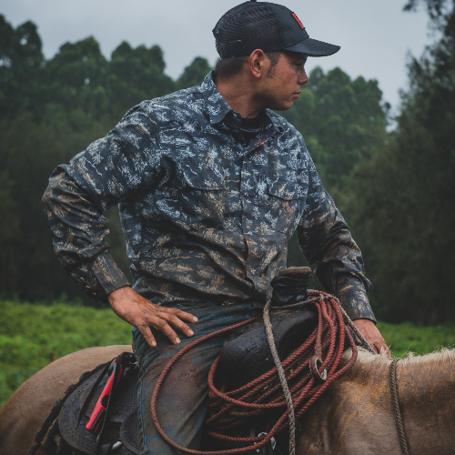 Man in camouflage jacket and cap riding a horse with trees in the background