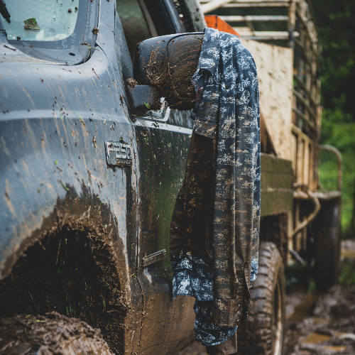 Person wearing camouflage pants standing next to a muddy vehicle in an outdoor setting