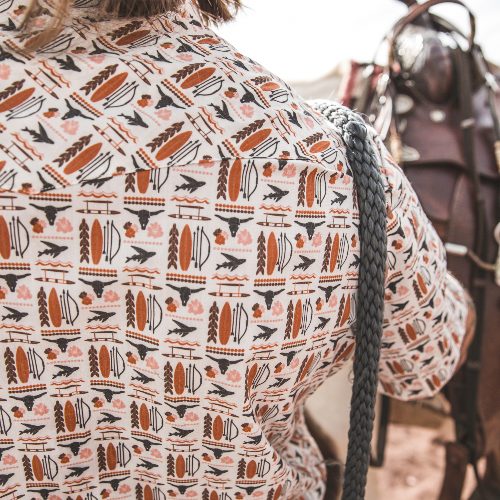 Person wearing a patterned shirt with a horse and rider in the background