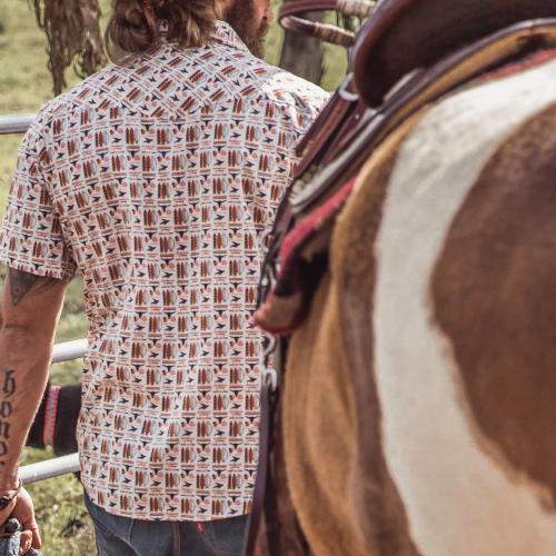 Person wearing a patterned shirt standing next to a horse in an outdoor setting