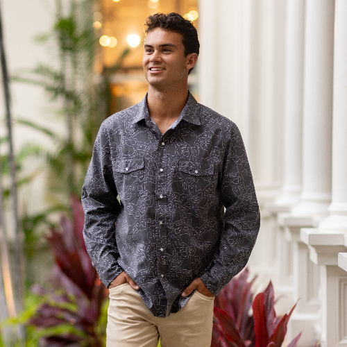 Man wearing a dark patterned shirt standing in an indoor setting with plants and architectural elements.