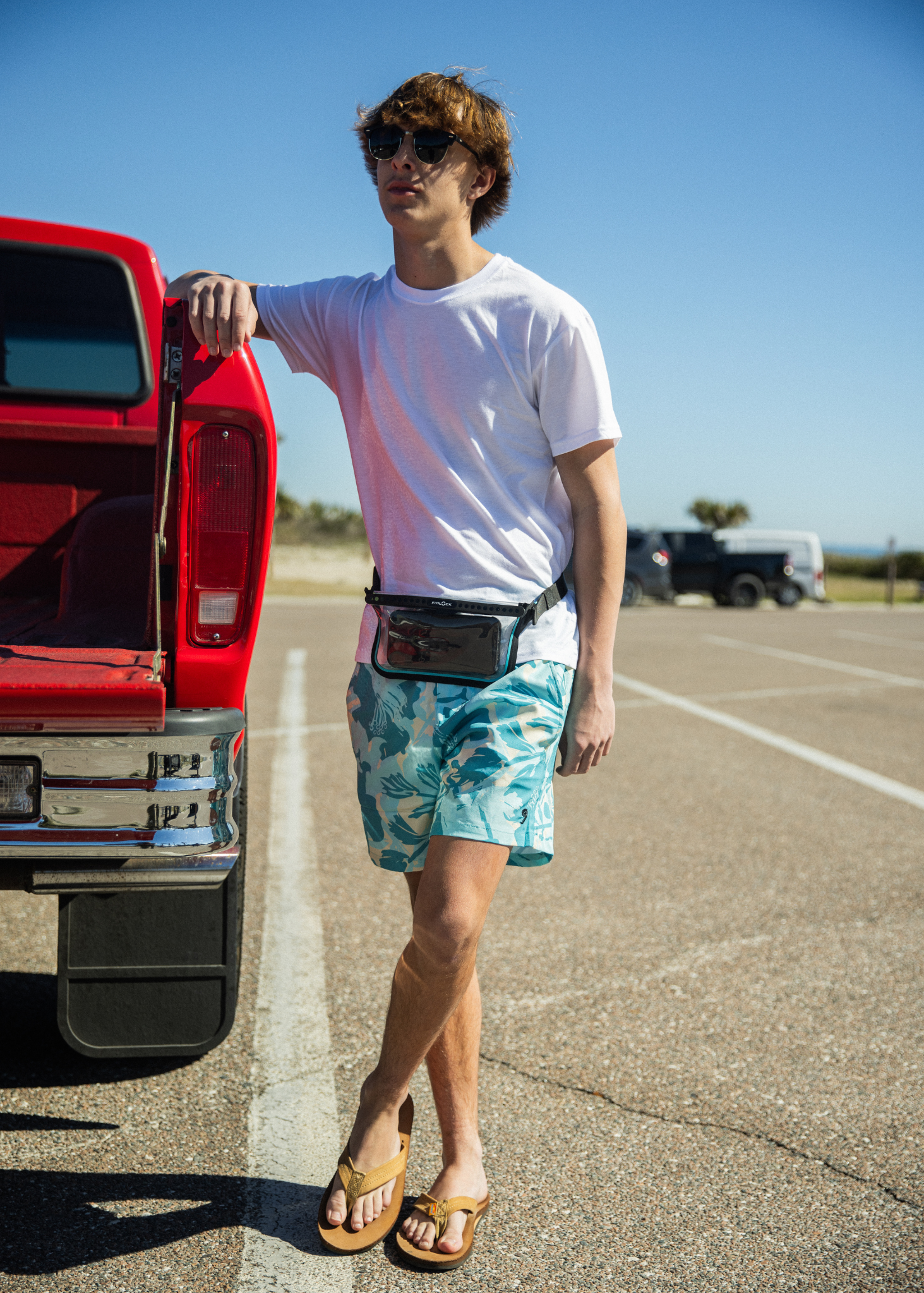 Man standing next to a red truck wearing a white t-shirt, green shorts, and sunglasses.