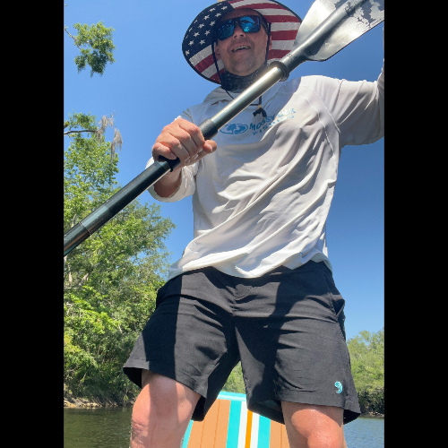 Man paddling a kayak on a sunny day with trees in the background